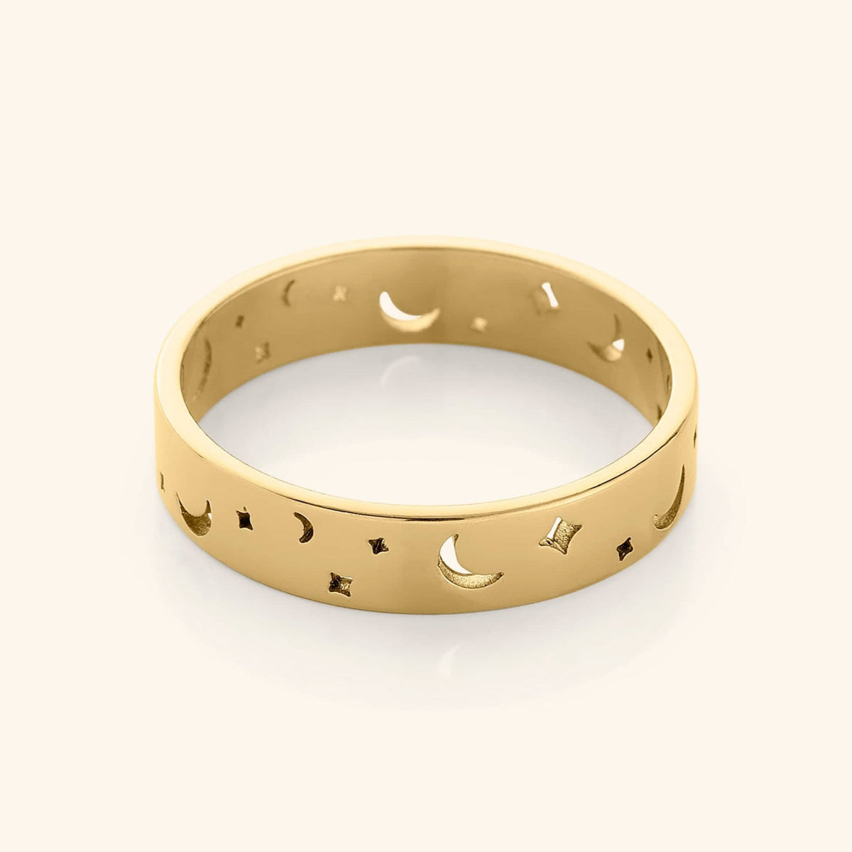 Gold band ring with cutout crescent moons and star shapes, displayed on a plain background.