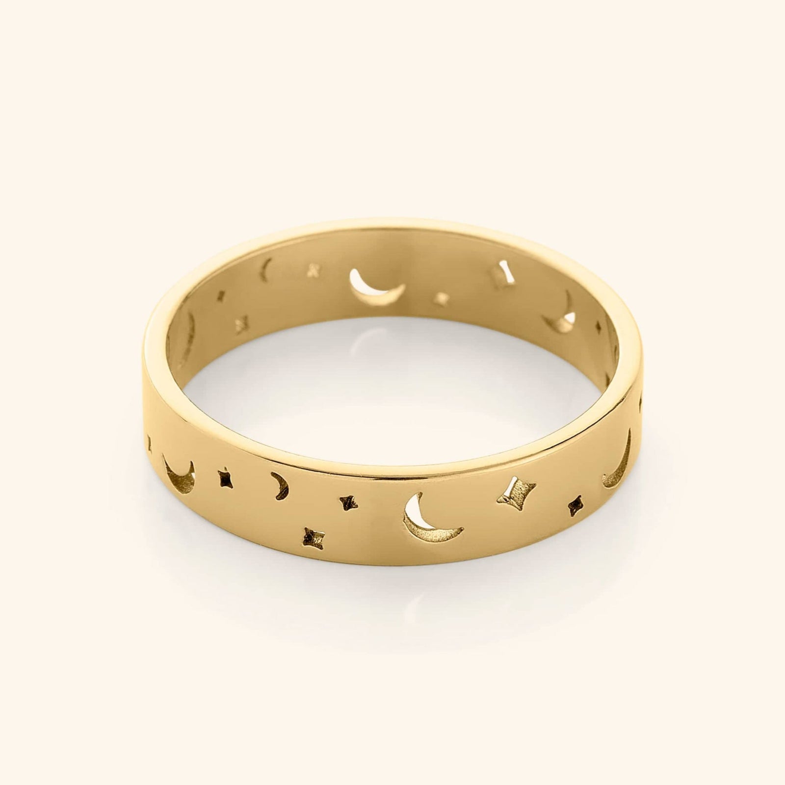 Gold band ring with cutout crescent moons and star shapes, displayed on a plain background.
