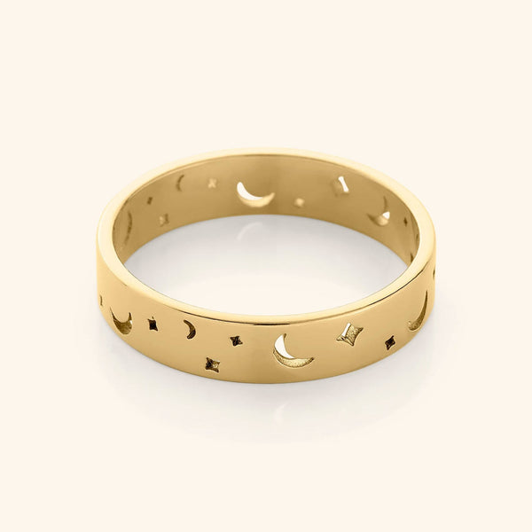 Gold band ring with cutout crescent moons and star shapes, displayed on a plain background.