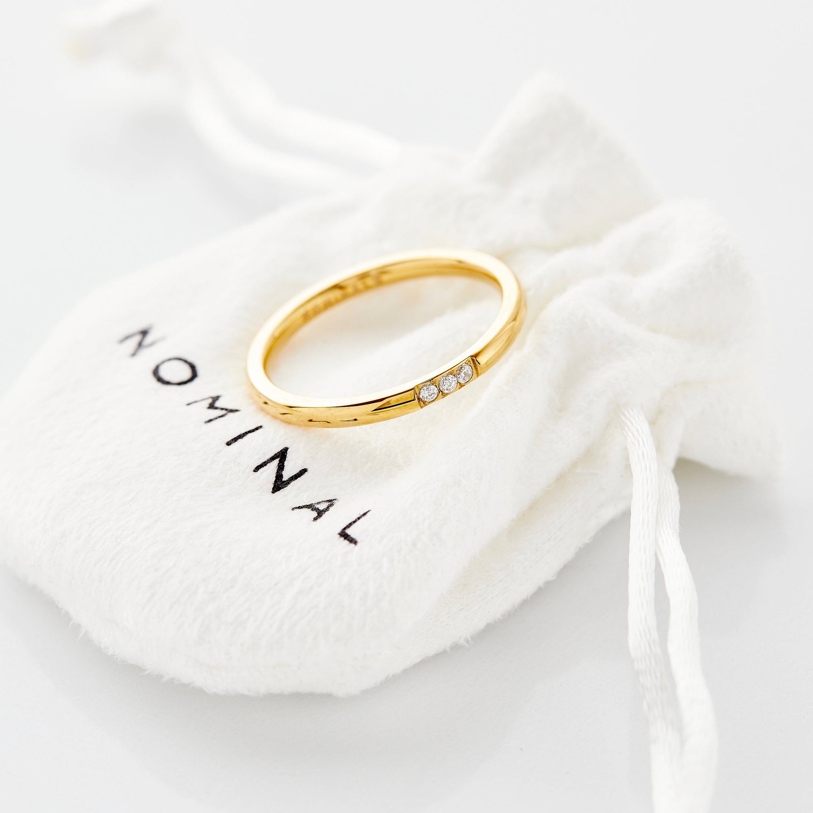 The gold Triple Bezel Ring resting on Nominal pouch.