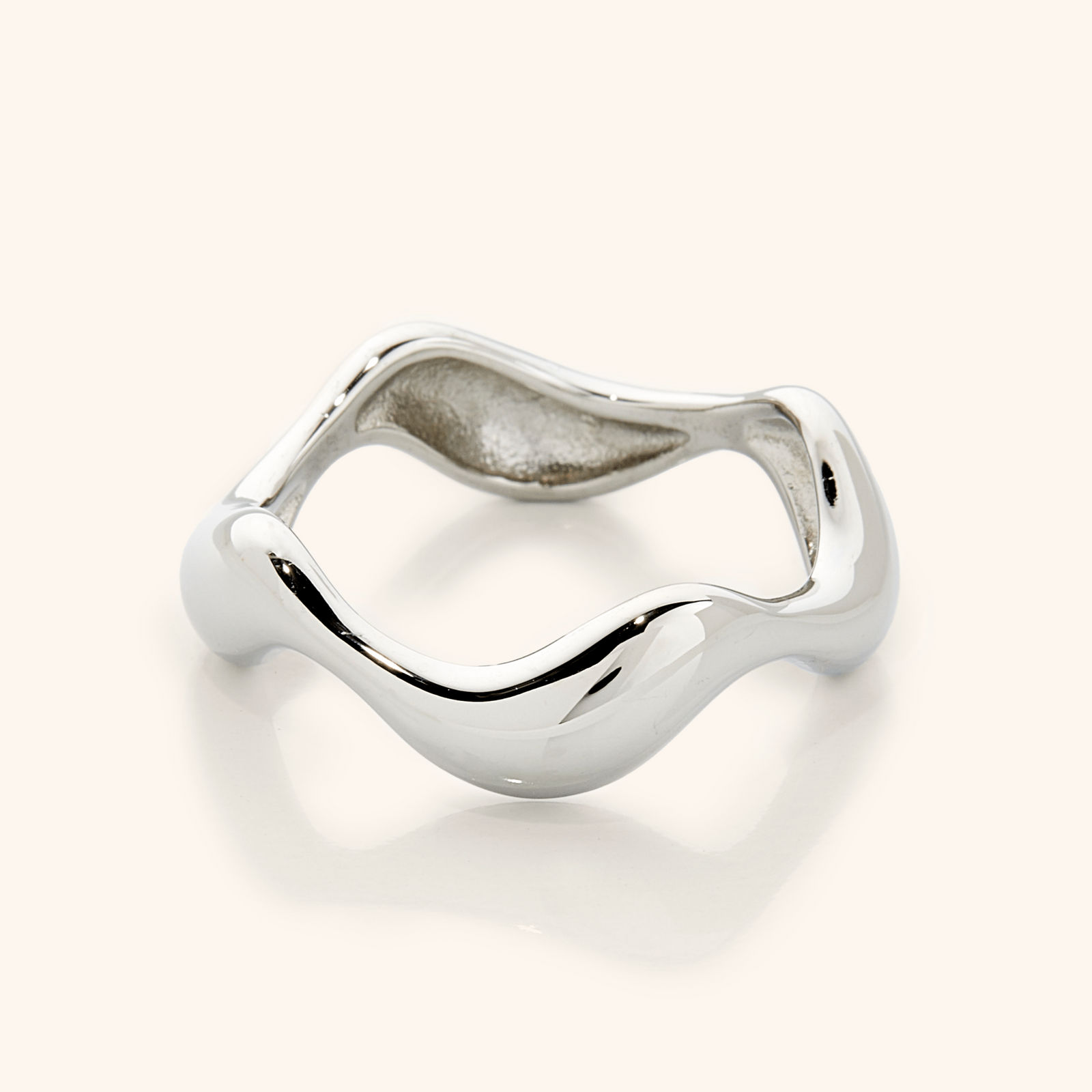 Close-up of a polished silver ring with a sculpted wavy band, photographed against a neutral background.