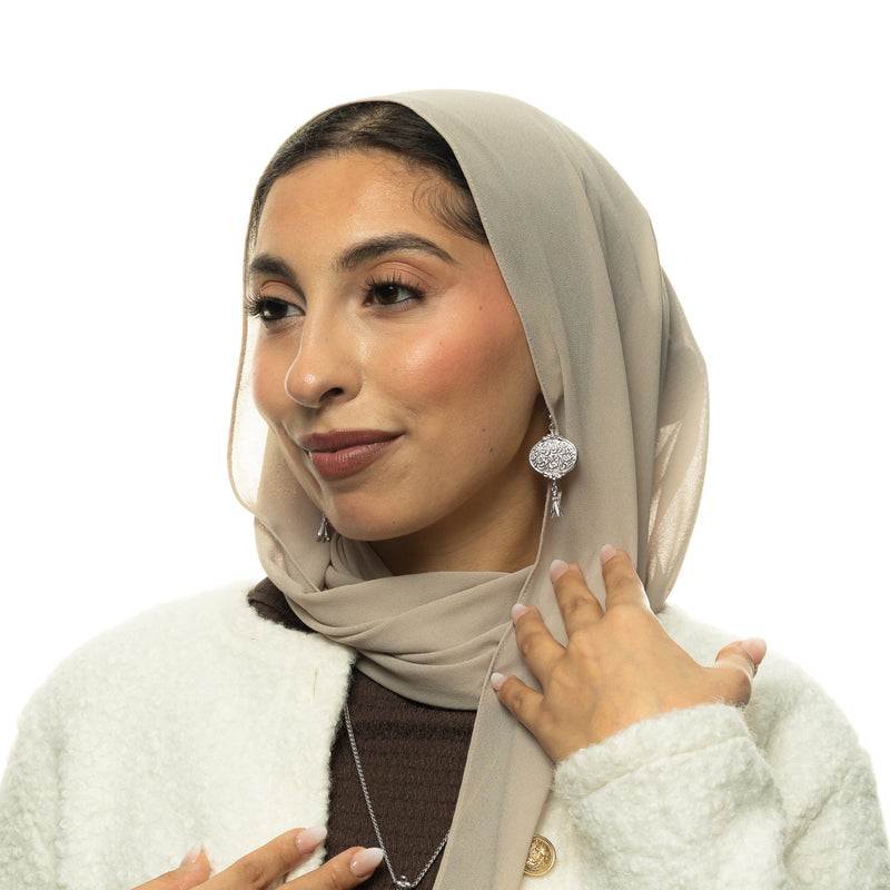 Model wearing the “Walk to Me pimage_ and I'll run to you” Medallion Earrings in silver pimage_ styled with a beige hijab.