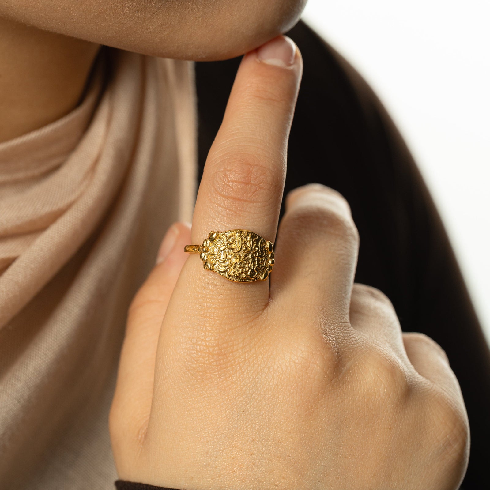 Photo of the gold "Walk to Me, and I'll run to you" Medallion Ring worn by the model on their index finger. The model touches their chin with their right index finger.