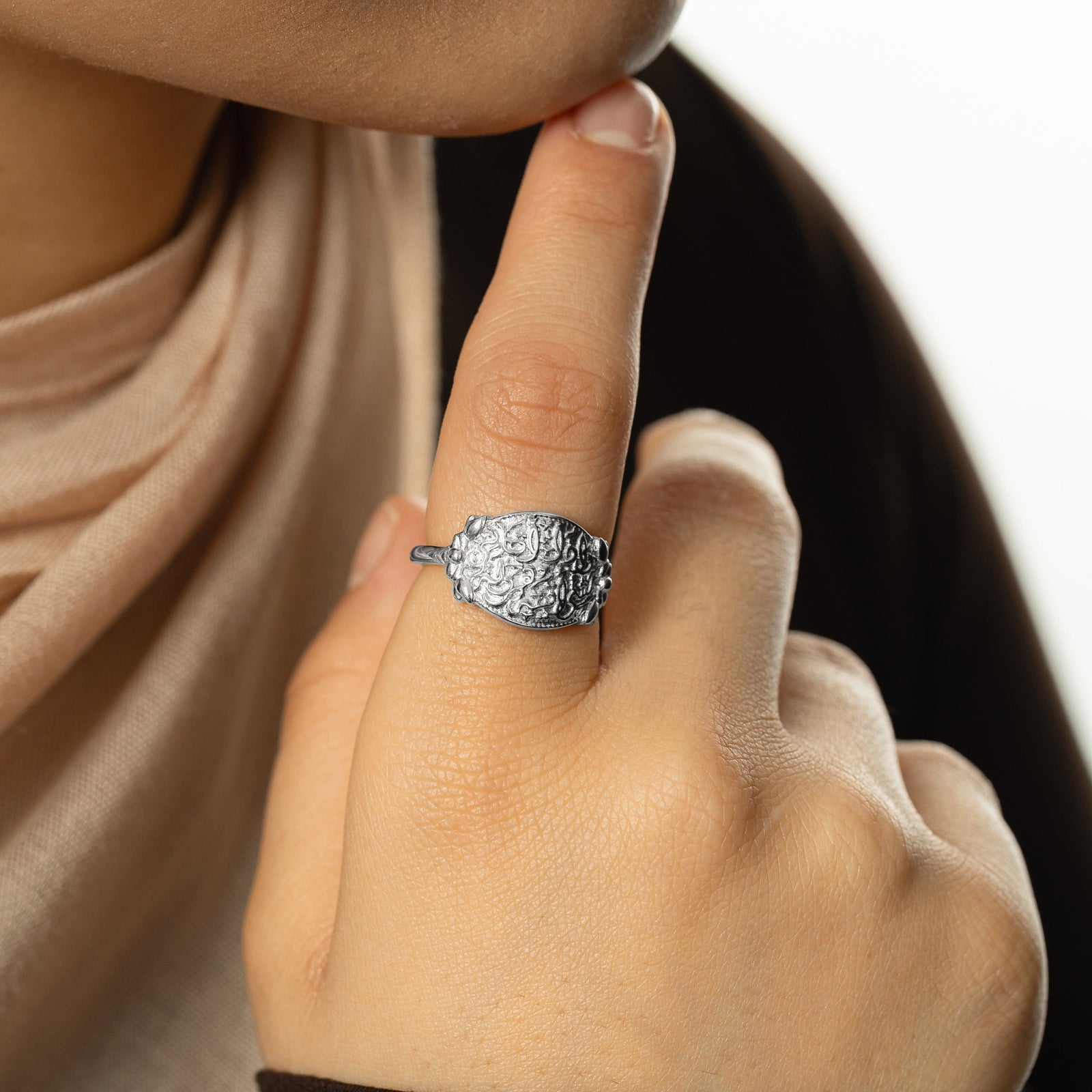 Photo of the silver "Walk to Me, and I'll run to you" Medallion Ring worn by the model on their index finger. The model touches their chin with their right index finger.