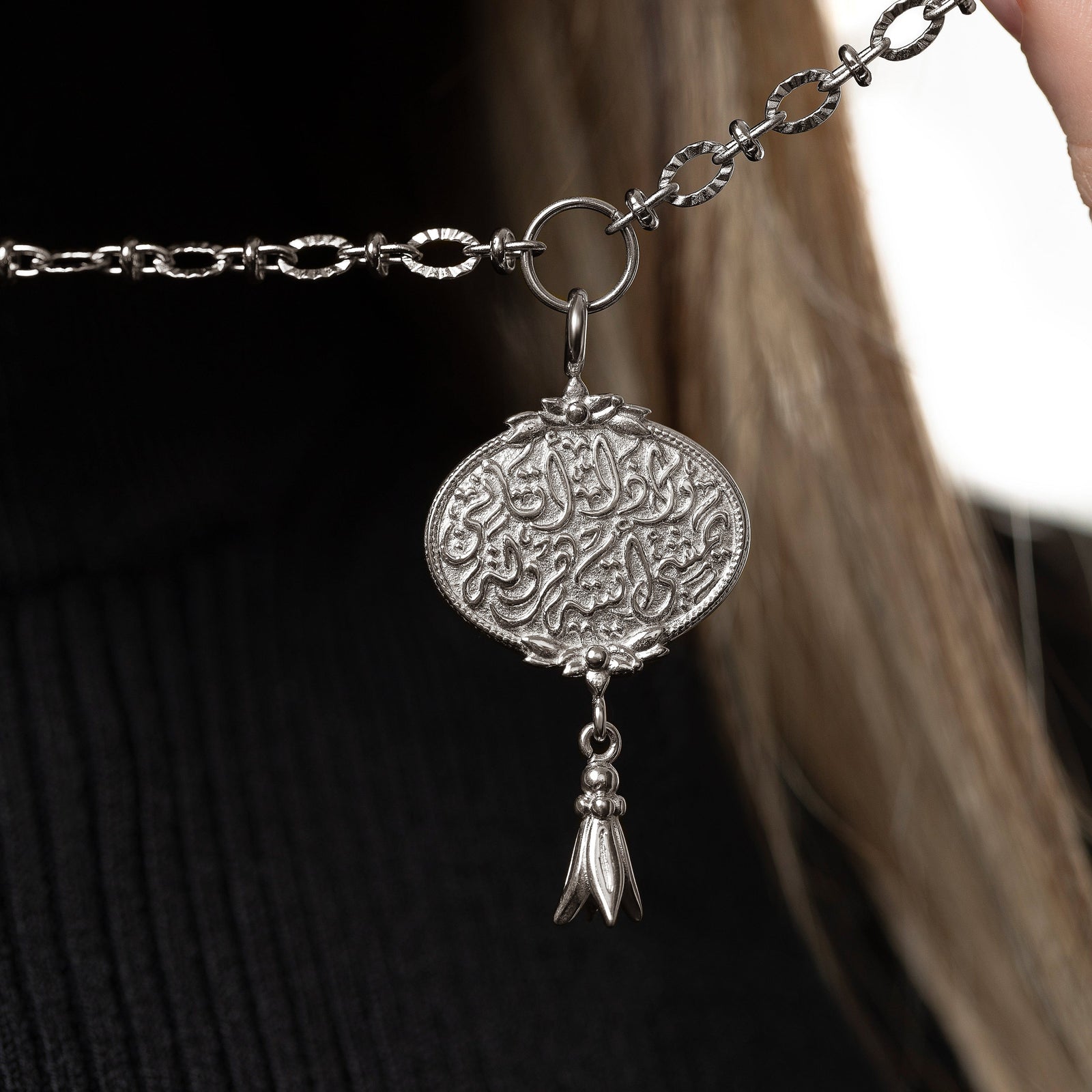 Model holds the chain to show the silver medallion-shaped pendant.