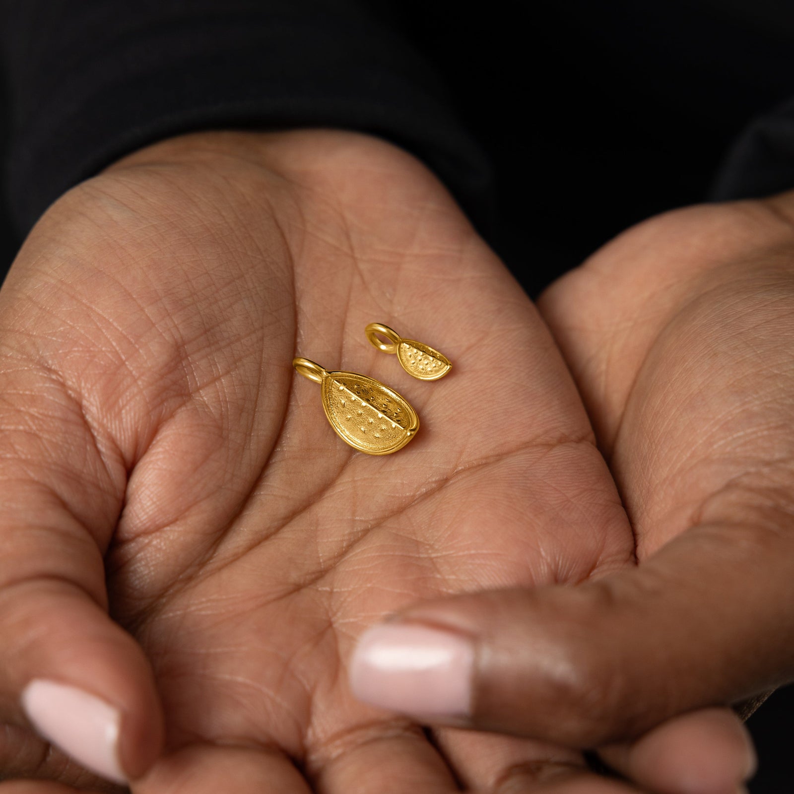 Close up of the gold Watermelon Earring Hoop Charms in different sizes on the model's palm.