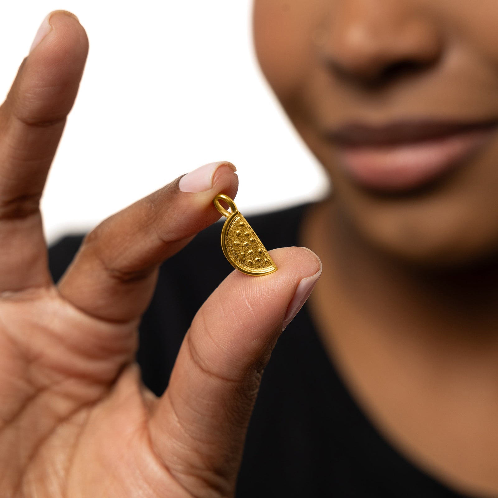 Close up of the gold Watermelon Earring Hoop Charm as held by the model between their finger.