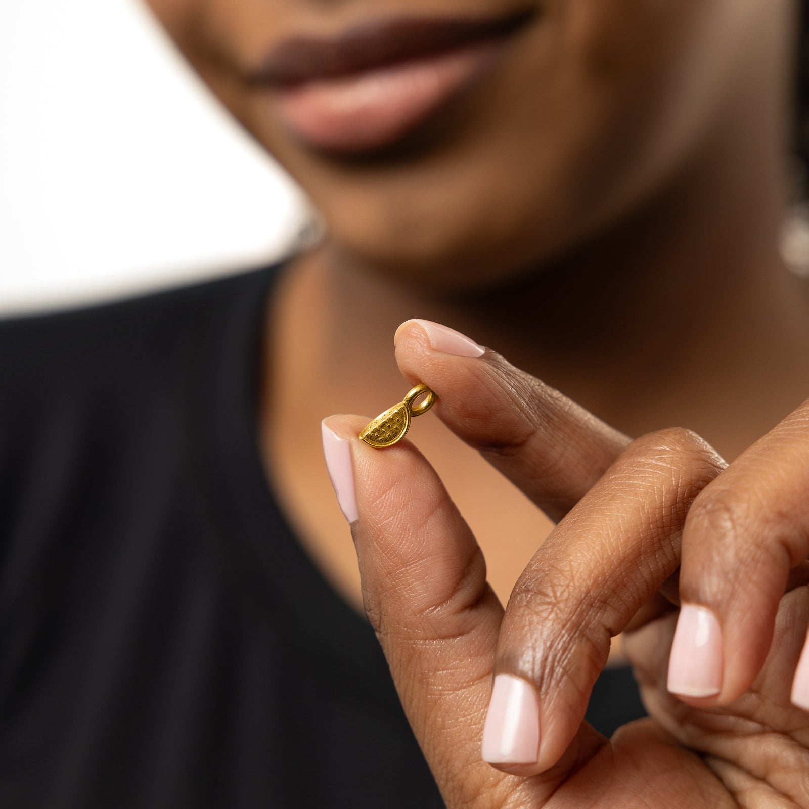 Close up of the gold Watermelon Earring Hoop Charm as the model holds it between their finger.