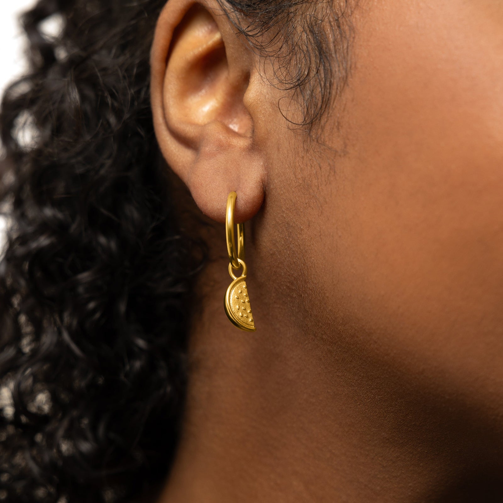 Close up of the gold Watermelon Earring Hoop Charm on a gold hoop earring as worn by the model on their right ear.
