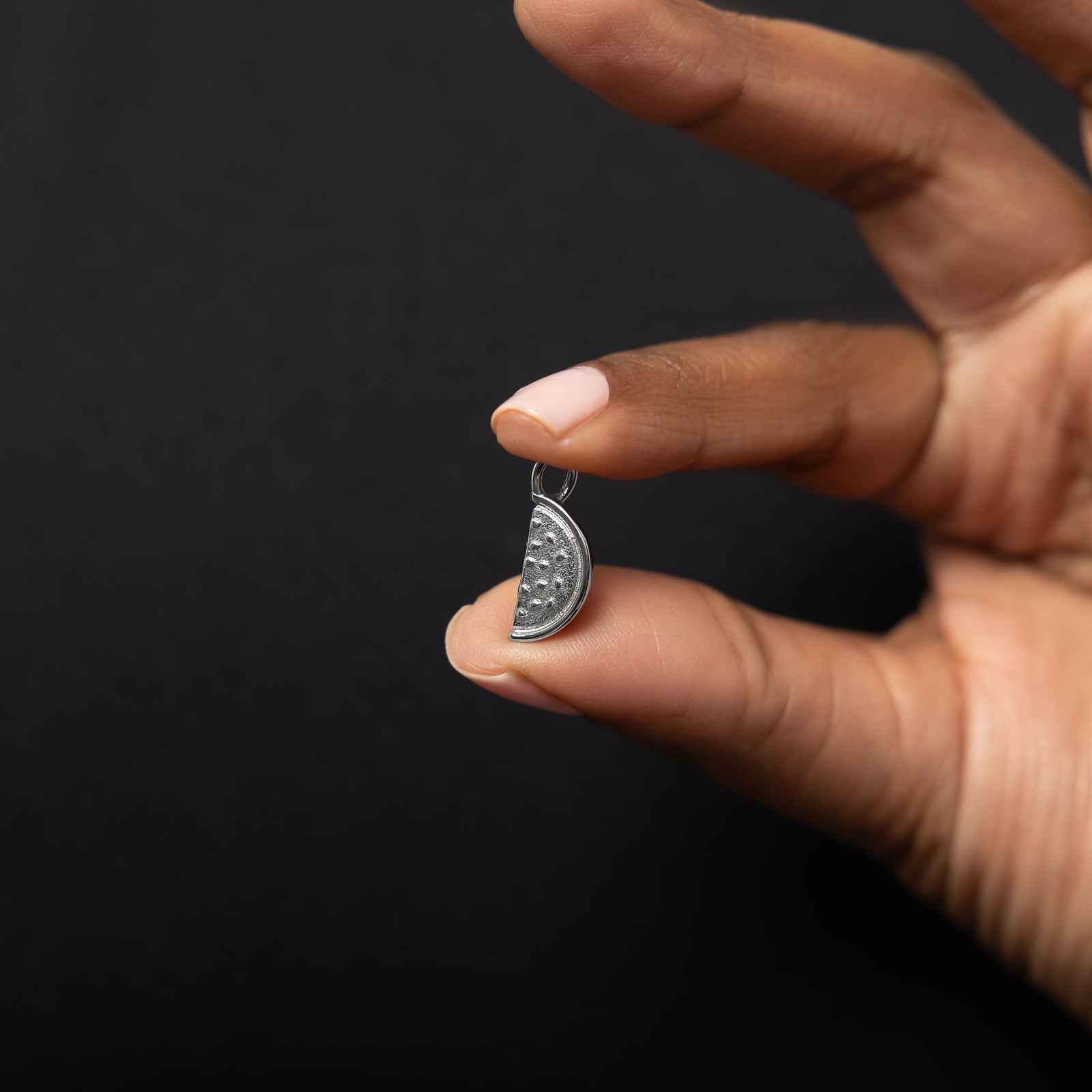 Close up the silver Watermelon Earring Hoop Charm as the model holds it between their finger.