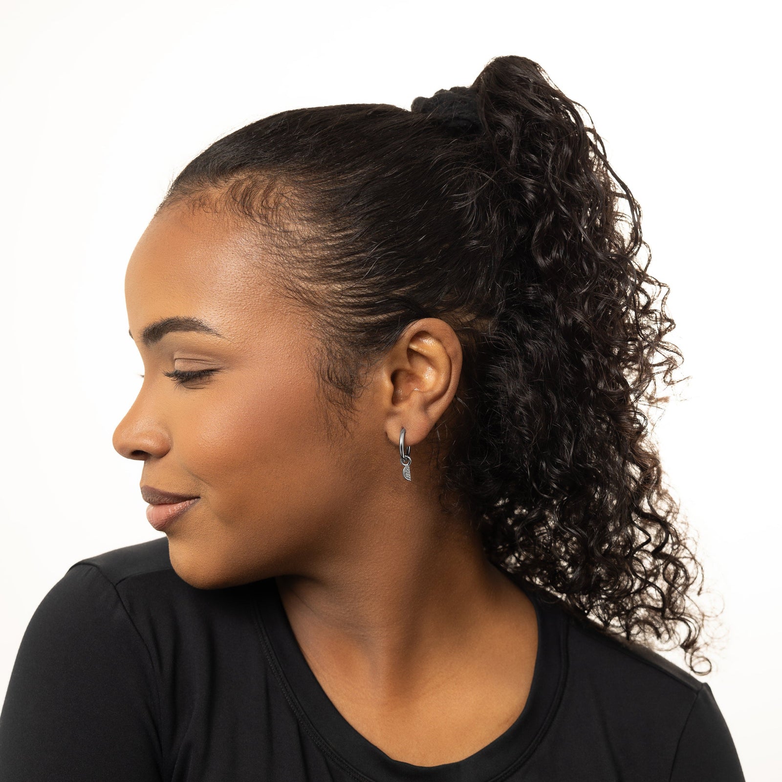 A model showcasing the silver Watermelon Hoops. The earrings are positioned on her earlobes, emphasizing the colorful watermelon slice design against a neutral background.