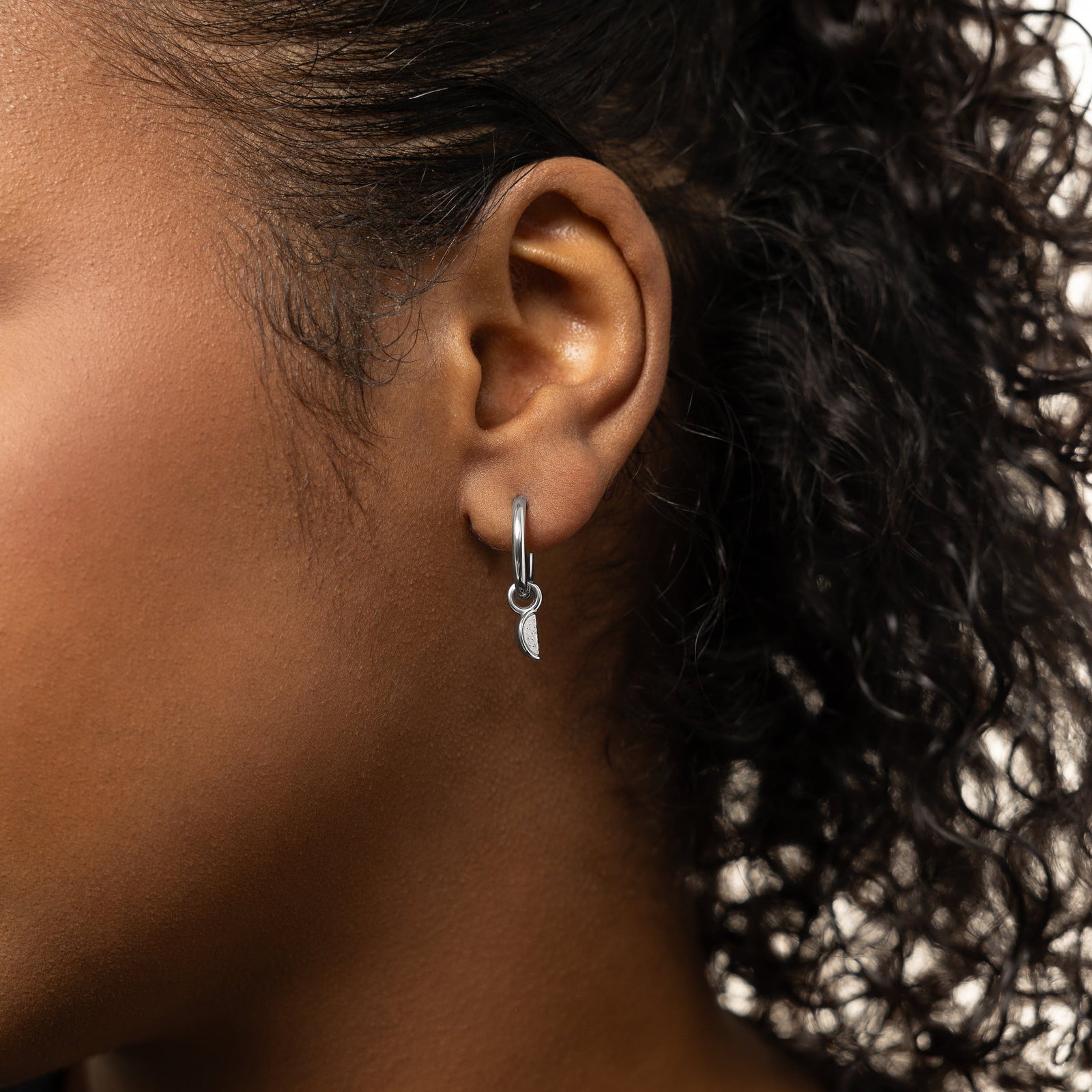 A model showcasing the silver Watermelon Hoops. The earrings are positioned on her earlobes, emphasizing the colorful watermelon slice design against a neutral background.