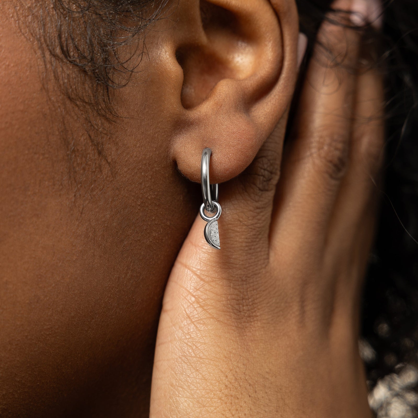 A model showcasing the silver Watermelon Hoops. The earrings are positioned on her earlobes, emphasizing the colorful watermelon slice design against a neutral background.