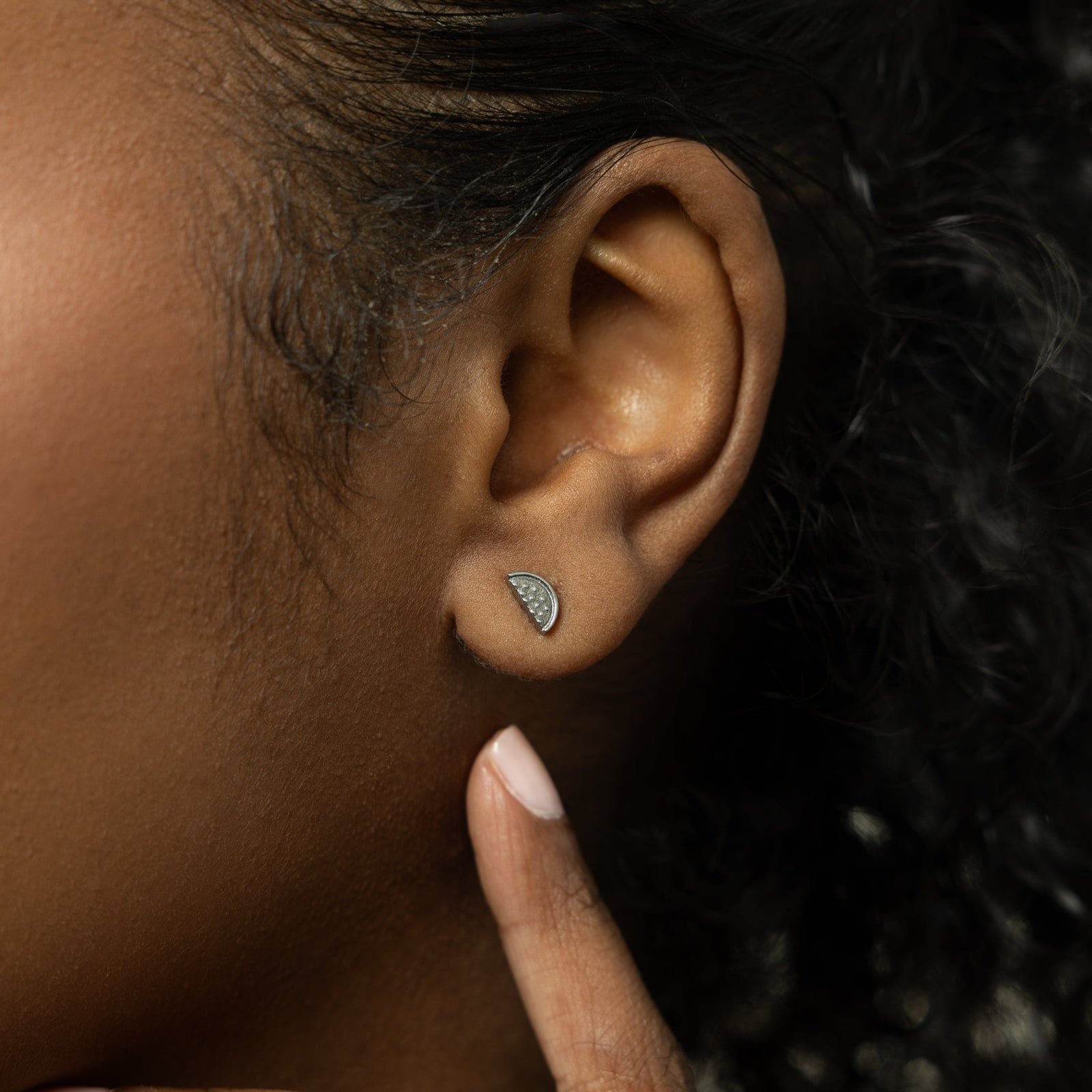A model showcasing the silver Watermelon Studs. The earrings are positioned on her earlobes, emphasizing the colorful watermelon slice design against a neutral background.