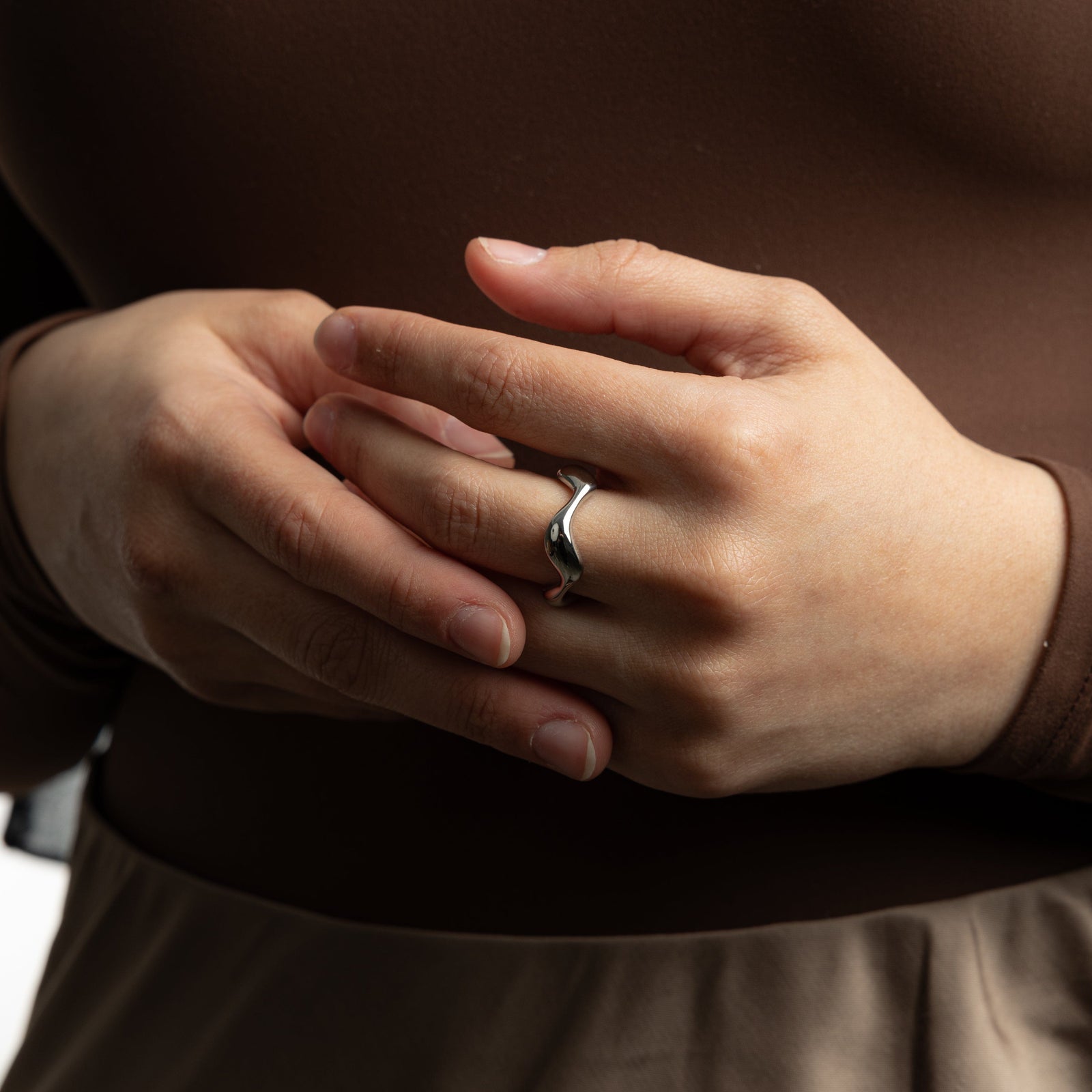 Hands shown close together with a silver wave ring on the middle finger, styled with a brown sleeve.