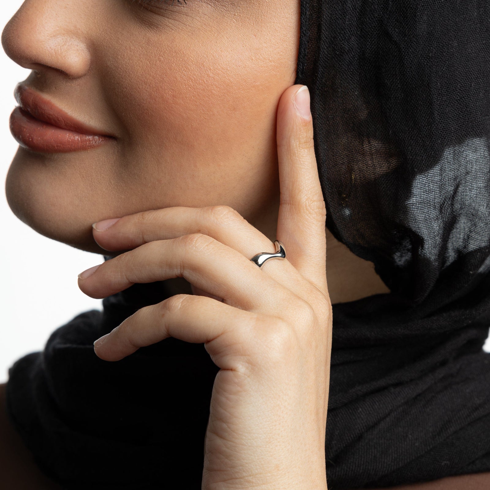 Woman wearing a silver wave ring on the middle finger with hand near her cheek
