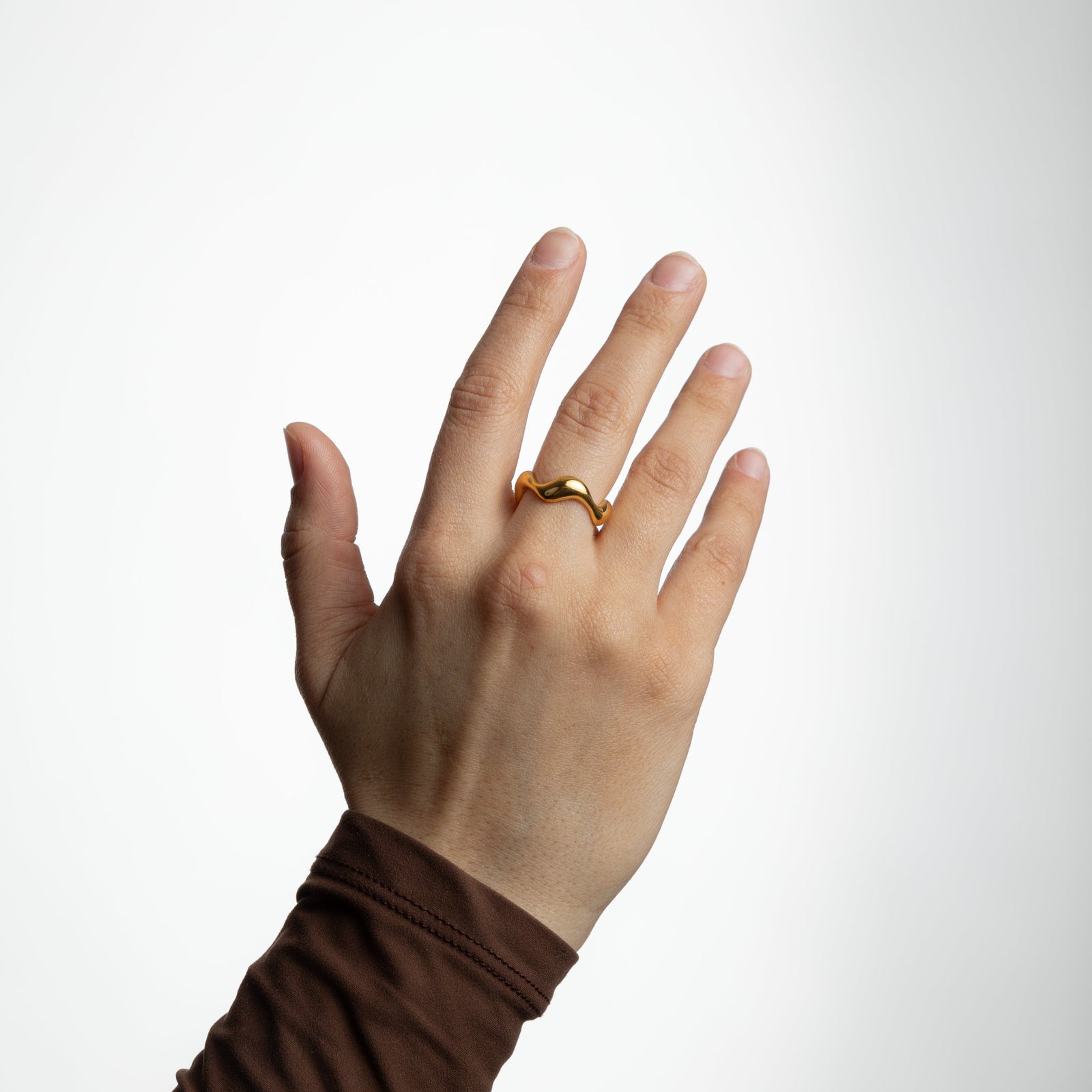 Open hand showing the gold wave ring on the middle finger, photographed against a white background.