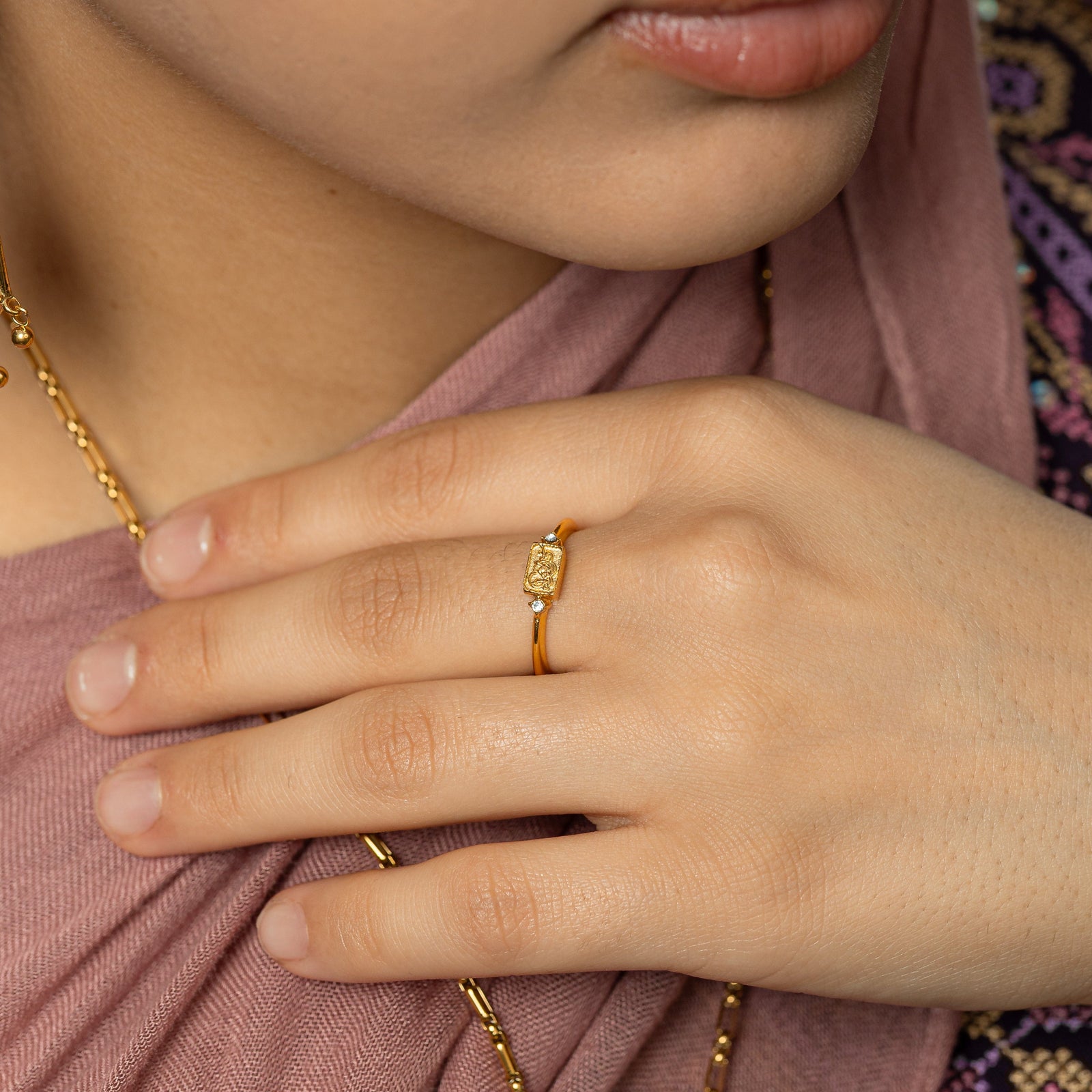 Model wearing the ring as they gently touch the chain of their necklace.
