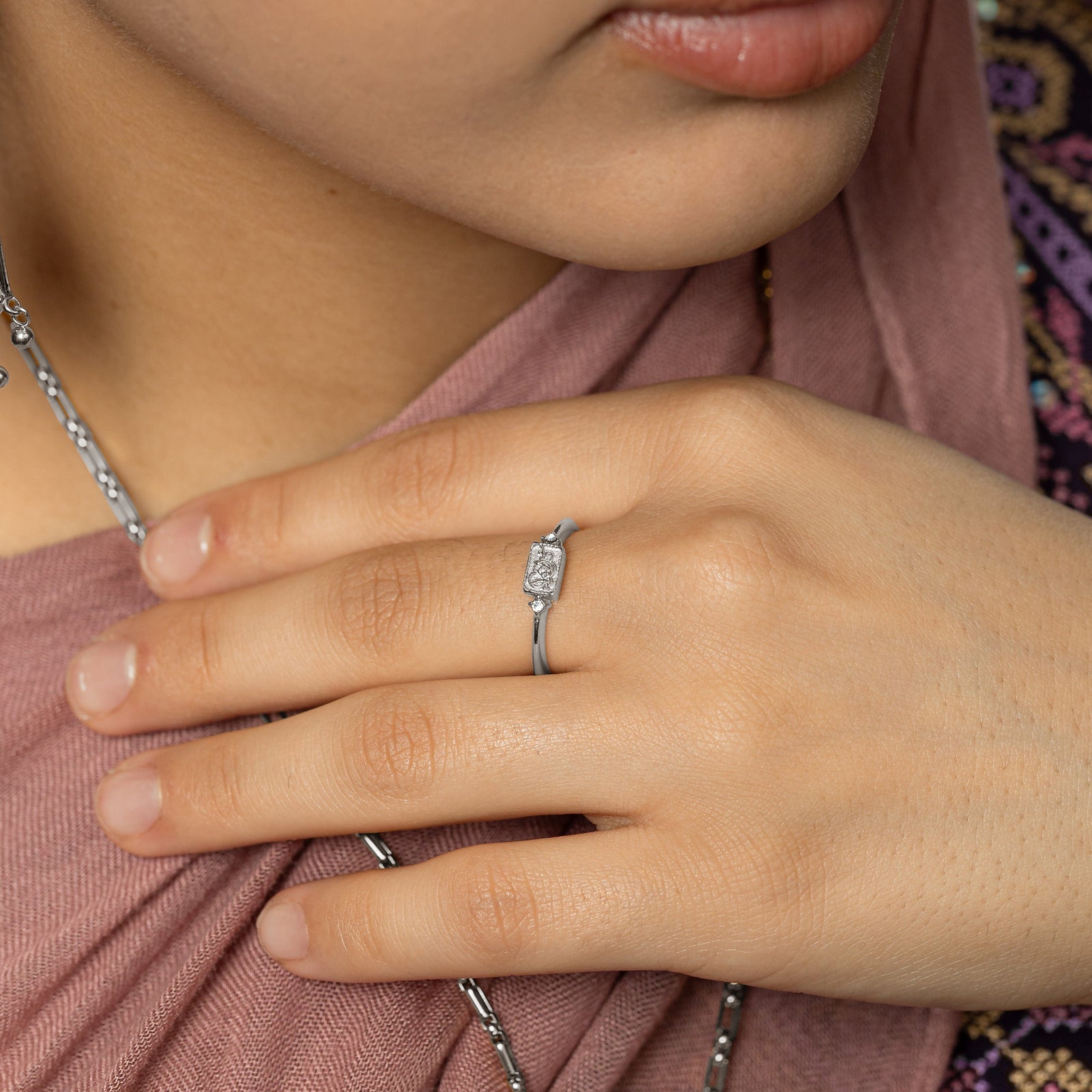 Model touches the chain of their silver necklace. Model is wearing the We Are Strong ring in silver.