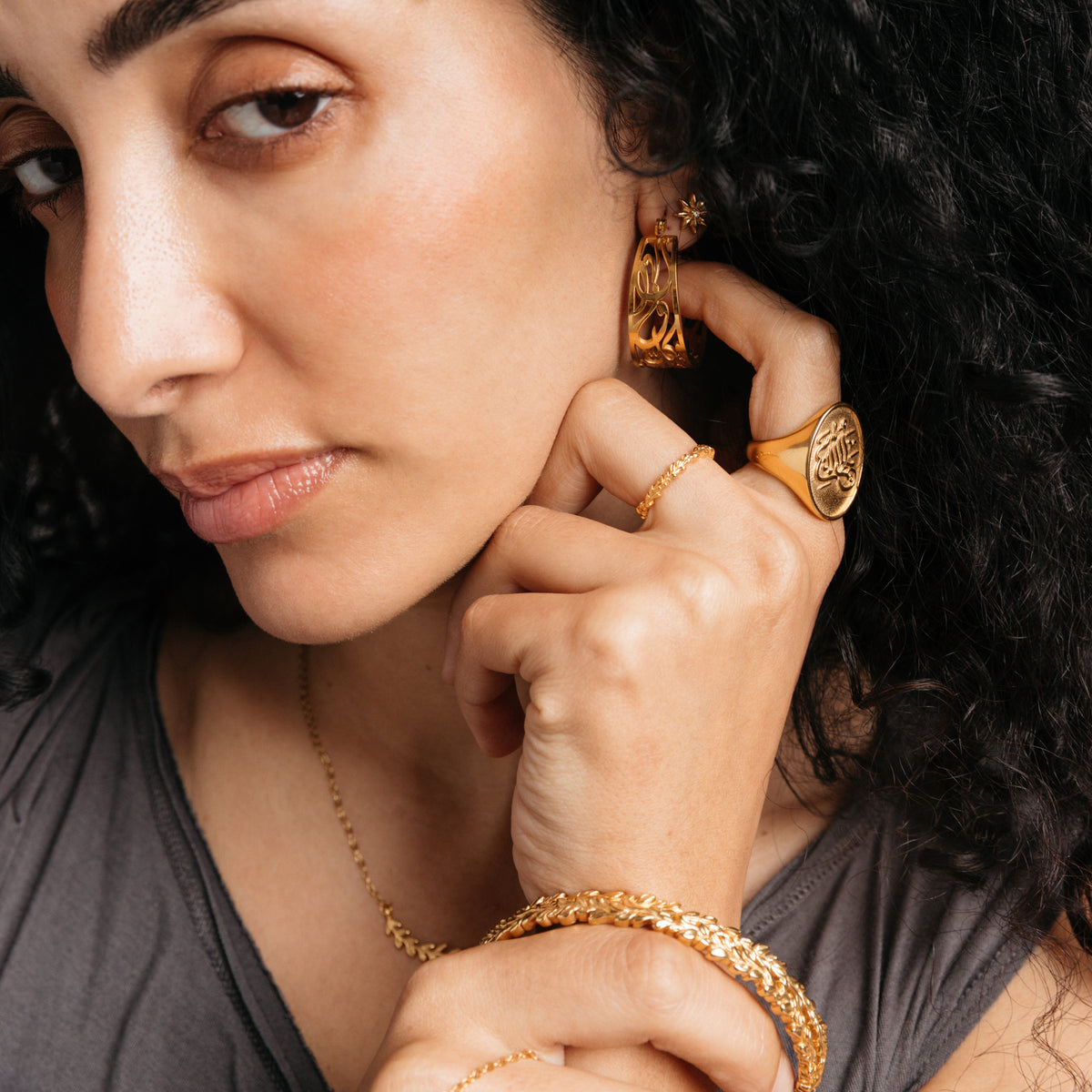 Model styled in 18k gold-plated Nominal jewelry featuring the Wrapped Olive Branch Ring paired with the Alhamdulillah Signet Ring, Weaving Olive Branch Bangle, and Calligraphy Hoops.