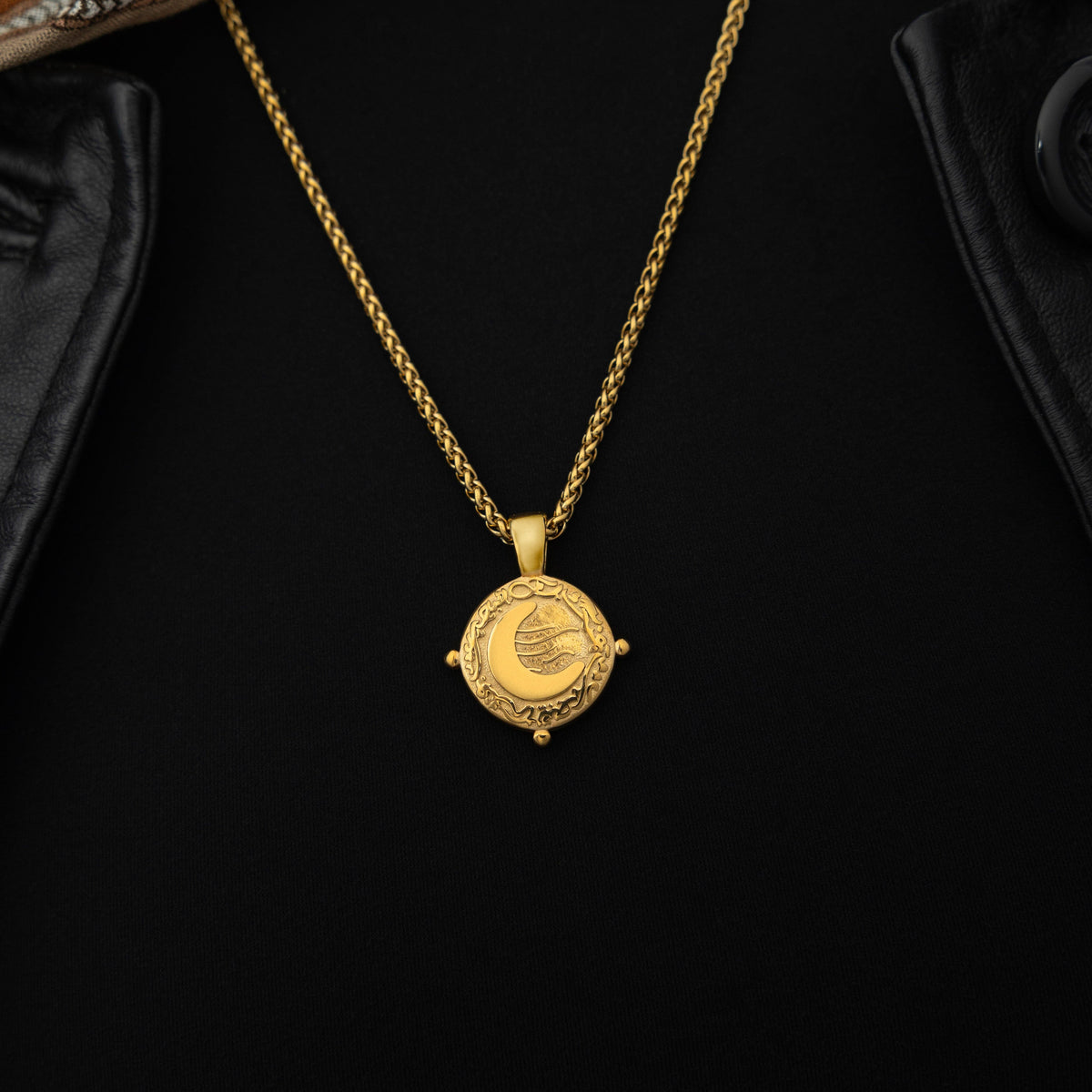 Gold necklace with a round pendant featuring the engraved phrase 'What you seek is seeking you' in Arabic calligraphy. The design includes a raised crescent moon and a flowing motif, framed with vine detailing and three small bead accents around the border. 