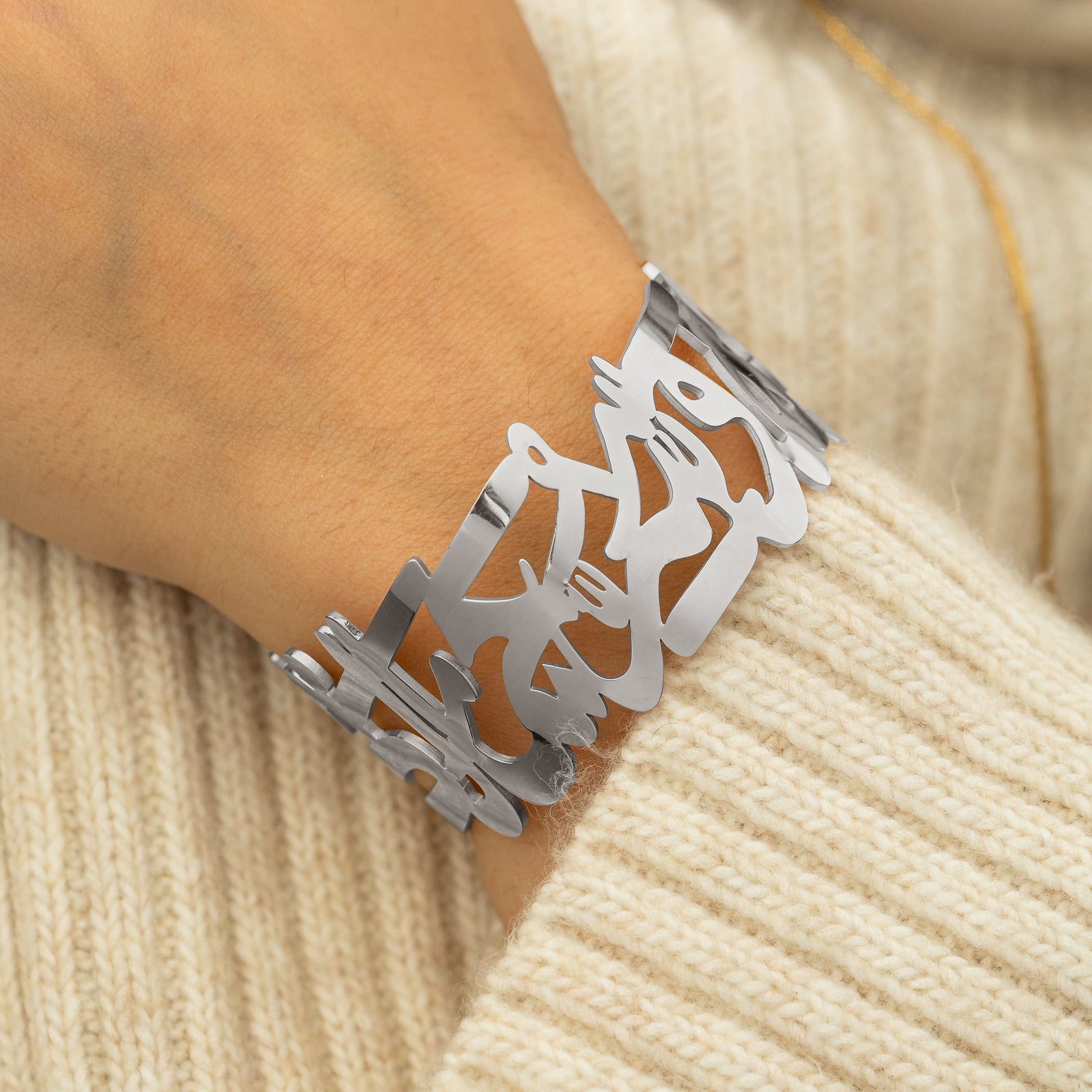 Close-up of the ‘What Makes You Different Makes You Beautiful’ Calligraphy Cuff in silver on a wrist, styled with a cream knit sweater.
