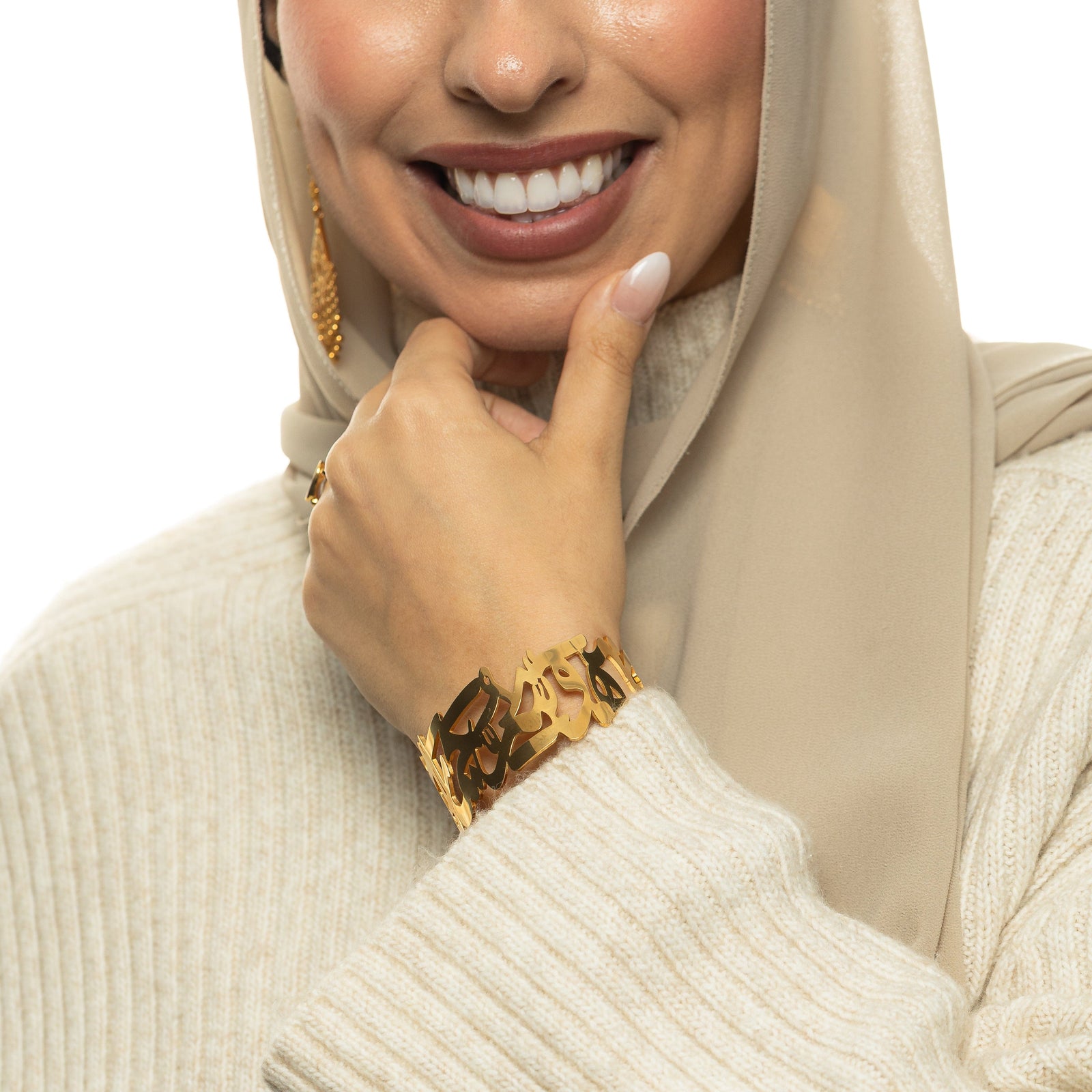 Model wearing the ‘What Makes You Different Makes You Beautiful’ Calligraphy Cuff in gold on the wrist, styled with a cream sweater and beige hijab.