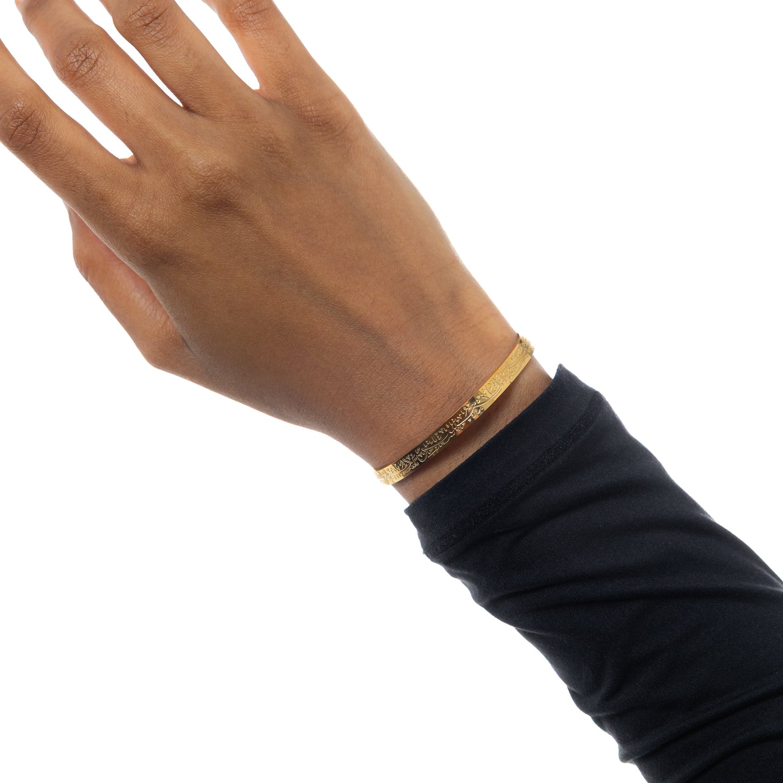 A model wearing the 18K gold-plated "With Hardship Comes Ease" Cuff V2. The cuff rests gracefully on her wrist, showcasing the embossed Arabic calligraphy against her skin, symbolizing resilience and hope.