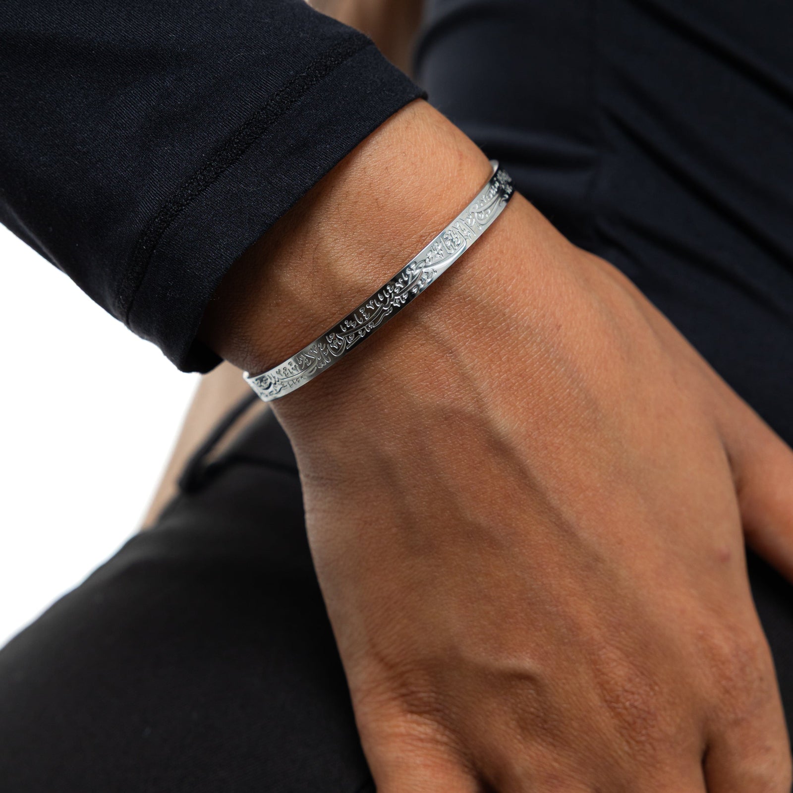 A model showcasing the silver "With Hardship Comes Ease" Cuff V2. The cuff encircles her wrist, emphasizing the detailed Arabic engraving and minimalist design against a neutral-toned outfit.