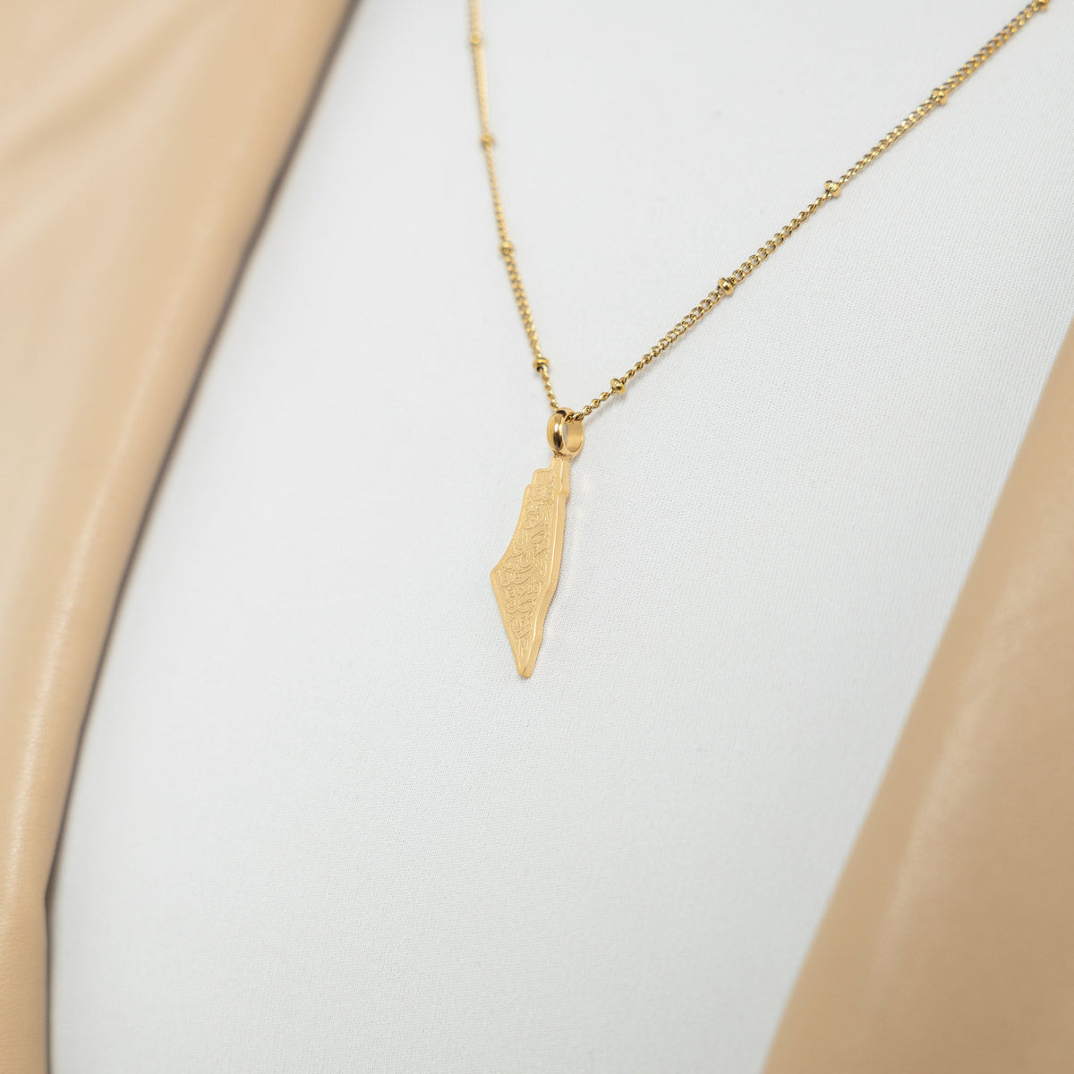 A model wearing the 18K gold-plated "With Hardship Comes Ease" Map Necklace. The necklace rests gracefully on her collarbone, highlighting the map pendant with Arabic calligraphy against a neutral-toned outfit.
