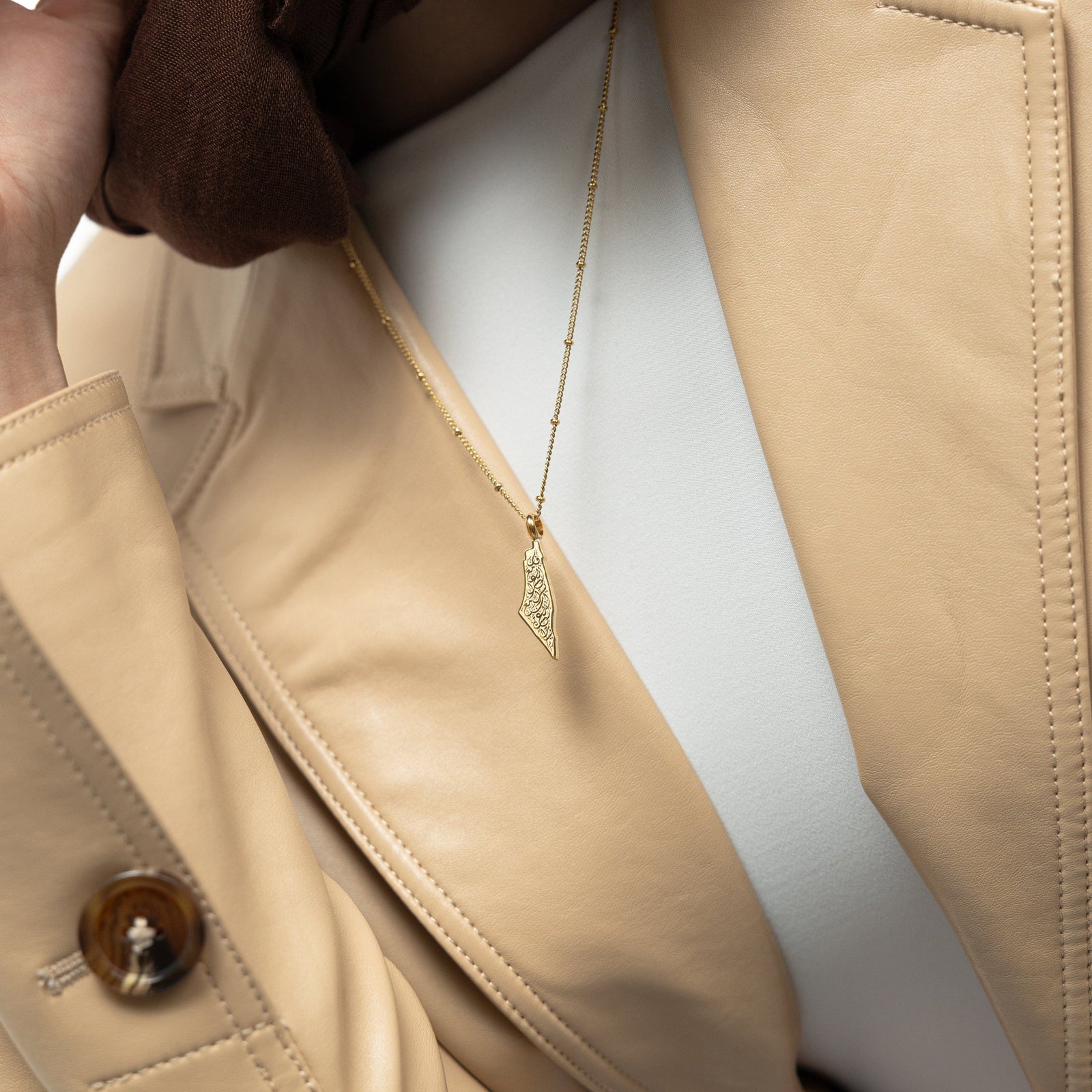 A model wearing the 18K gold-plated "With Hardship Comes Ease" Map Necklace. The necklace rests gracefully on her collarbone, highlighting the map pendant with Arabic calligraphy against a neutral-toned outfit.