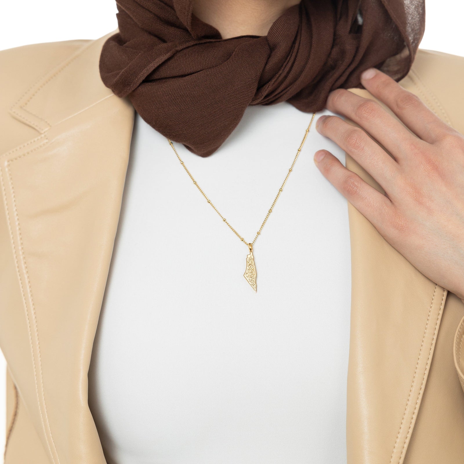 A model wearing the 18K gold-plated "With Hardship Comes Ease" Map Necklace. The necklace rests gracefully on her collarbone, highlighting the map pendant with Arabic calligraphy against a neutral-toned outfit.