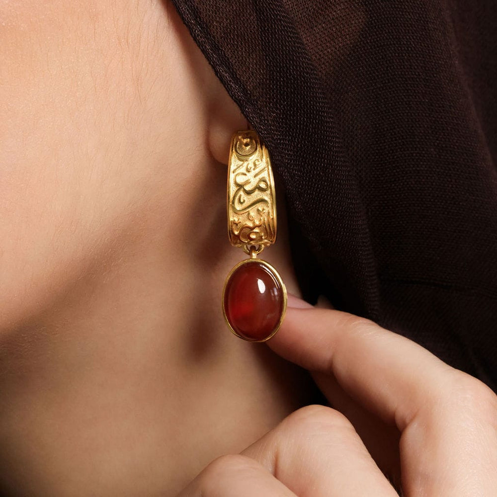 Close up of the gold "With Hardship Comes Ease" Earring as worn by the model.