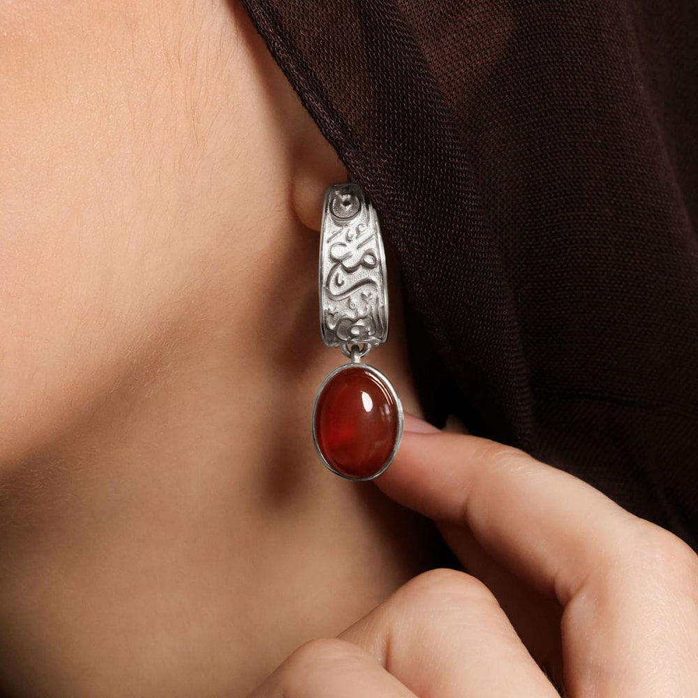 Close up of the silver "With Hardship Comes Ease" Earring as worn by the model.