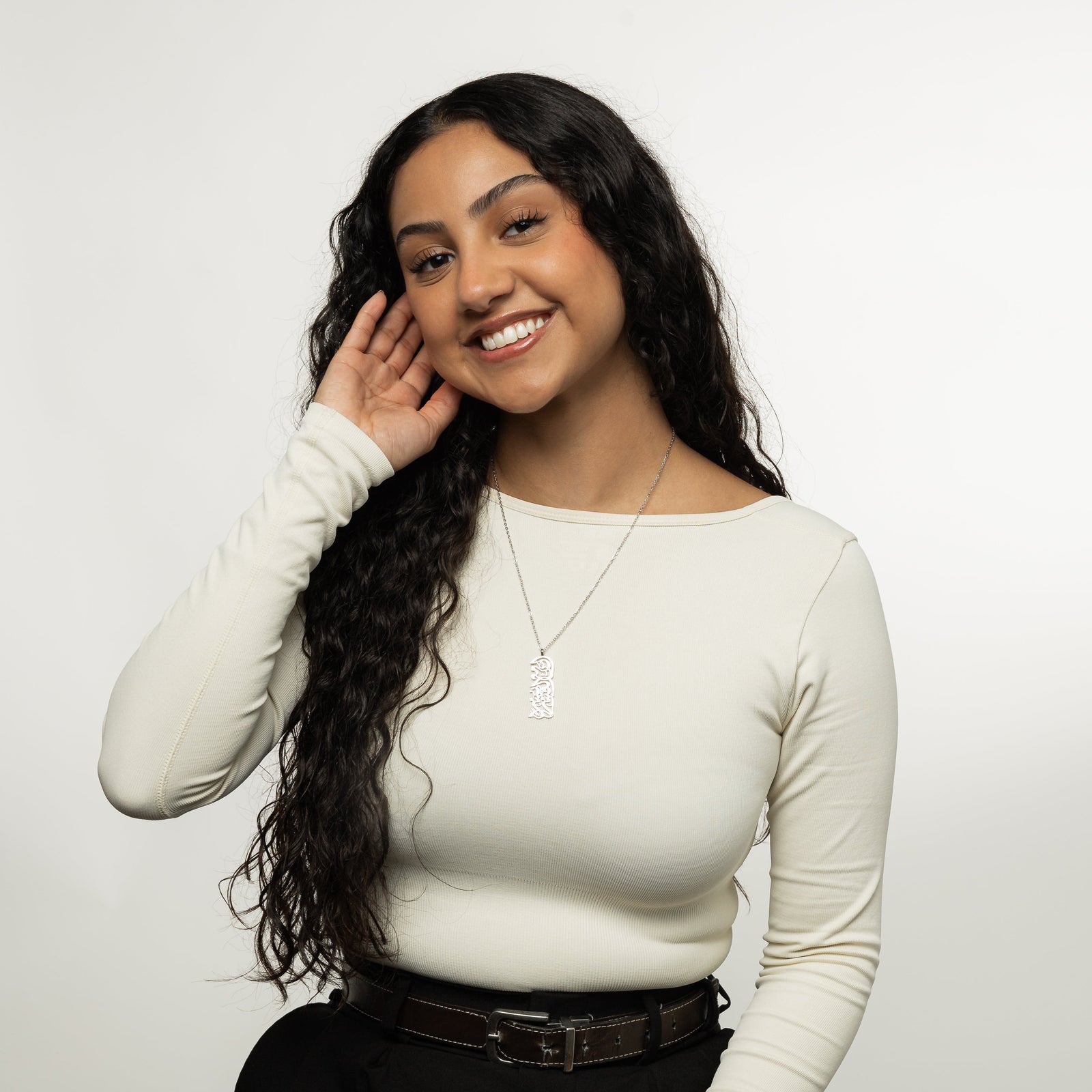 A model showcasing the silver "With Hardship Comes Ease" Calligraphy Necklace. The pendant hangs elegantly from her neck, emphasizing the detailed Arabic engraving against a neutral-toned outfit.