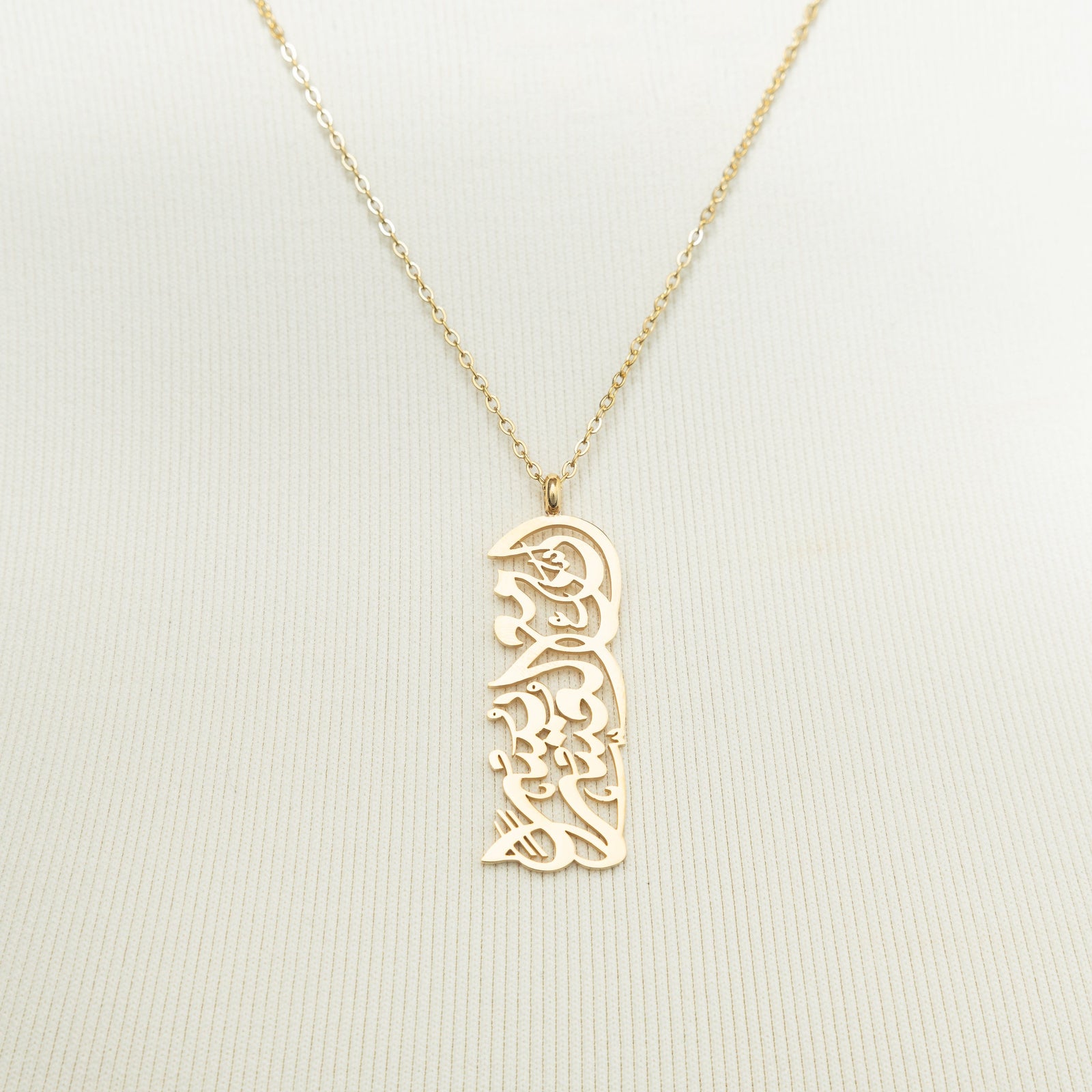 A close-up of the "With Hardship Comes Ease" Calligraphy Necklace in 18K gold plating. The necklace features a rectangular pendant engraved with the Arabic verse "إِنَّ مَعَ الْعُسْرِ يُسْرًا" ("Verily, with hardship comes ease") from the Qur'an, suspended from a delicate chain.