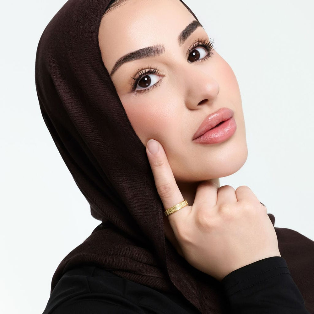 Close up of the model's face with her right index finger touching their cheek to show the gold "With Hardship Comes Ease" Ring V2 | Women they are wearing.