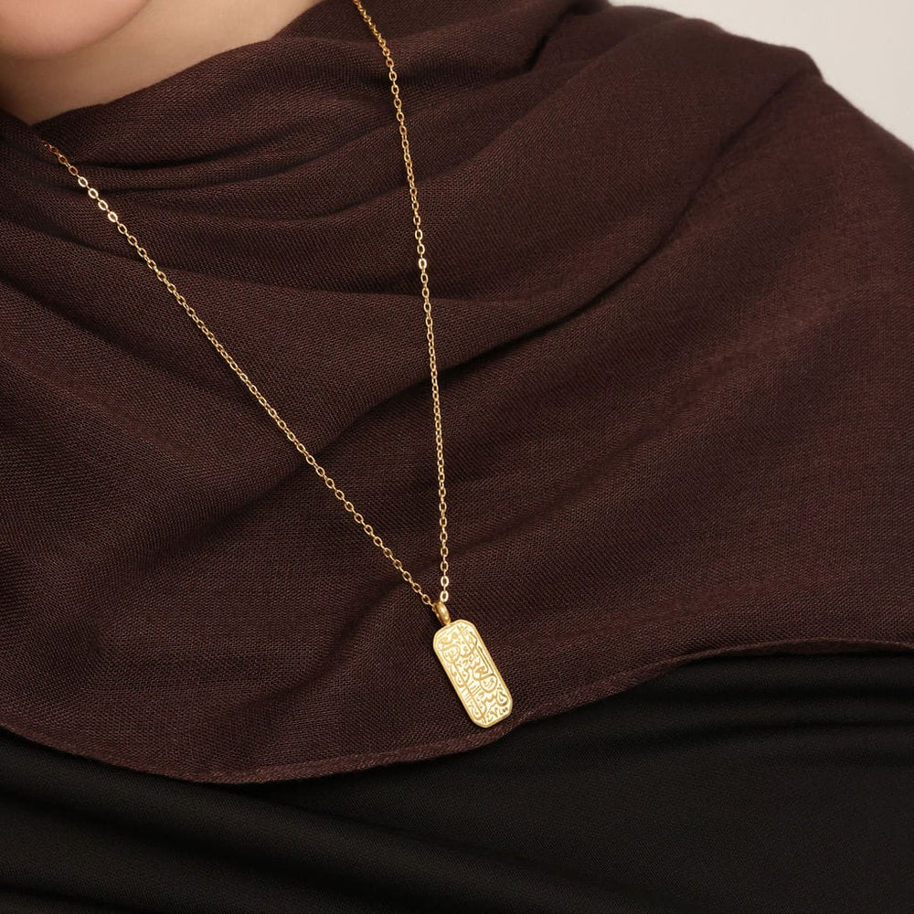 Close up of the gold "With Hardship Comes Ease" Tag | Women as worn by the model.