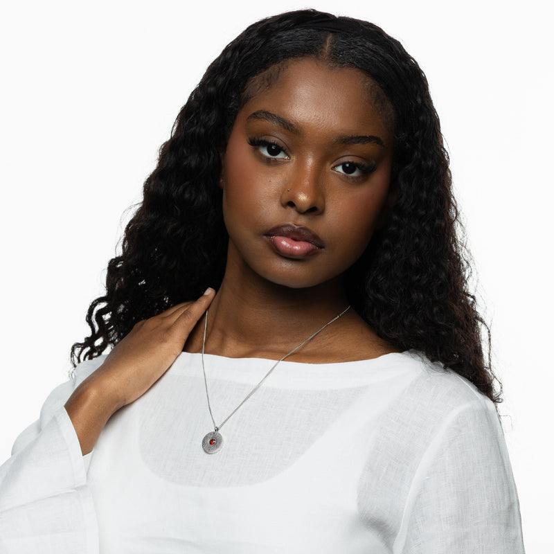 Woman wearing the silver medallion necklace with red agate pendant pimage_ styled with a white top pimage_ hand resting near her collarbone.