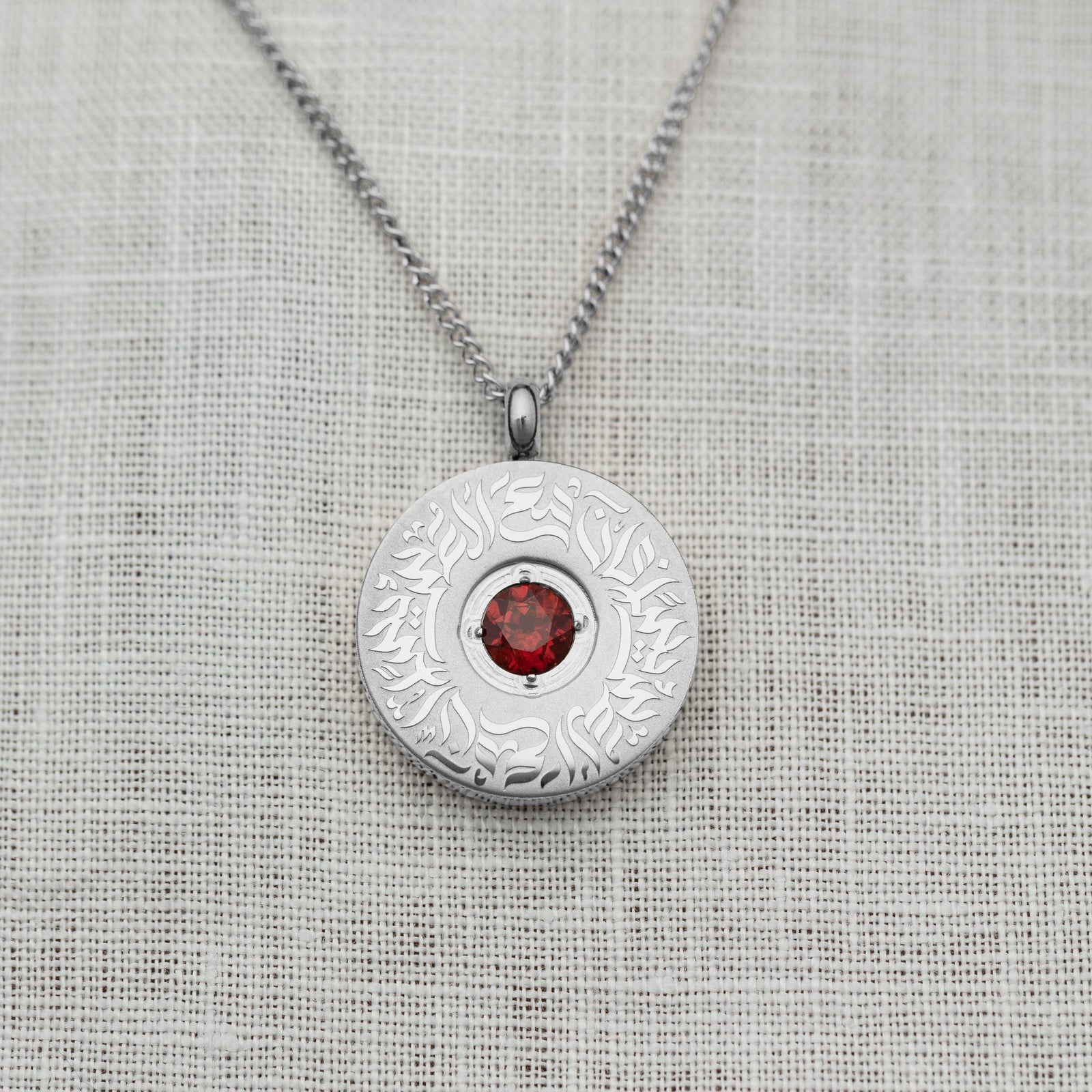 Close-up of the silver medallion necklace with a polished red agate stone at the center, encircled by detailed Arabic calligraphy.