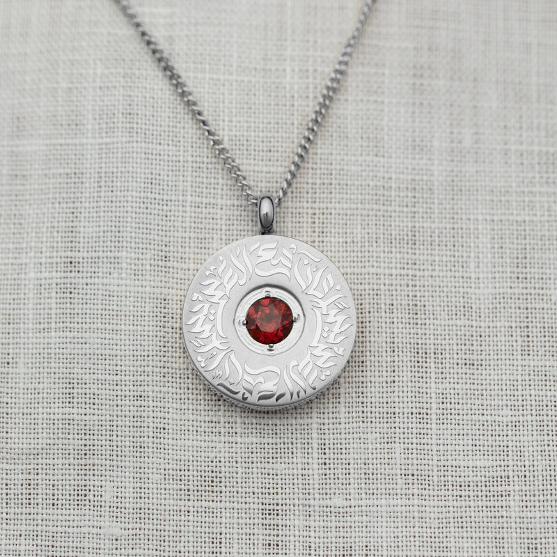 Close-up of the silver medallion necklace with a polished red agate stone at the center pimage_ encircled by detailed Arabic calligraphy.