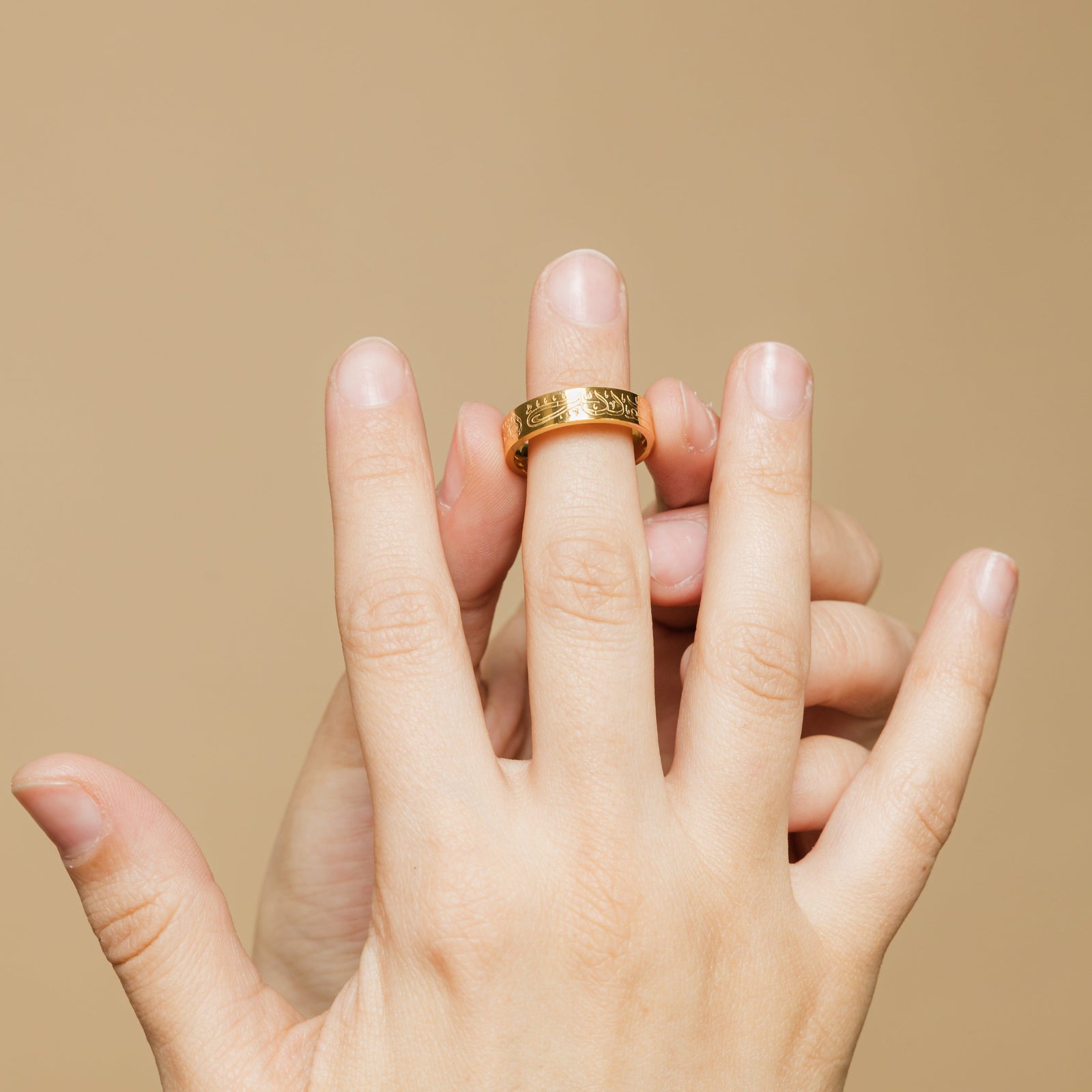 Close-up of hand slipping the gold Alhamdulillah ring onto the middle finger, showing the engraved calligraphy details.