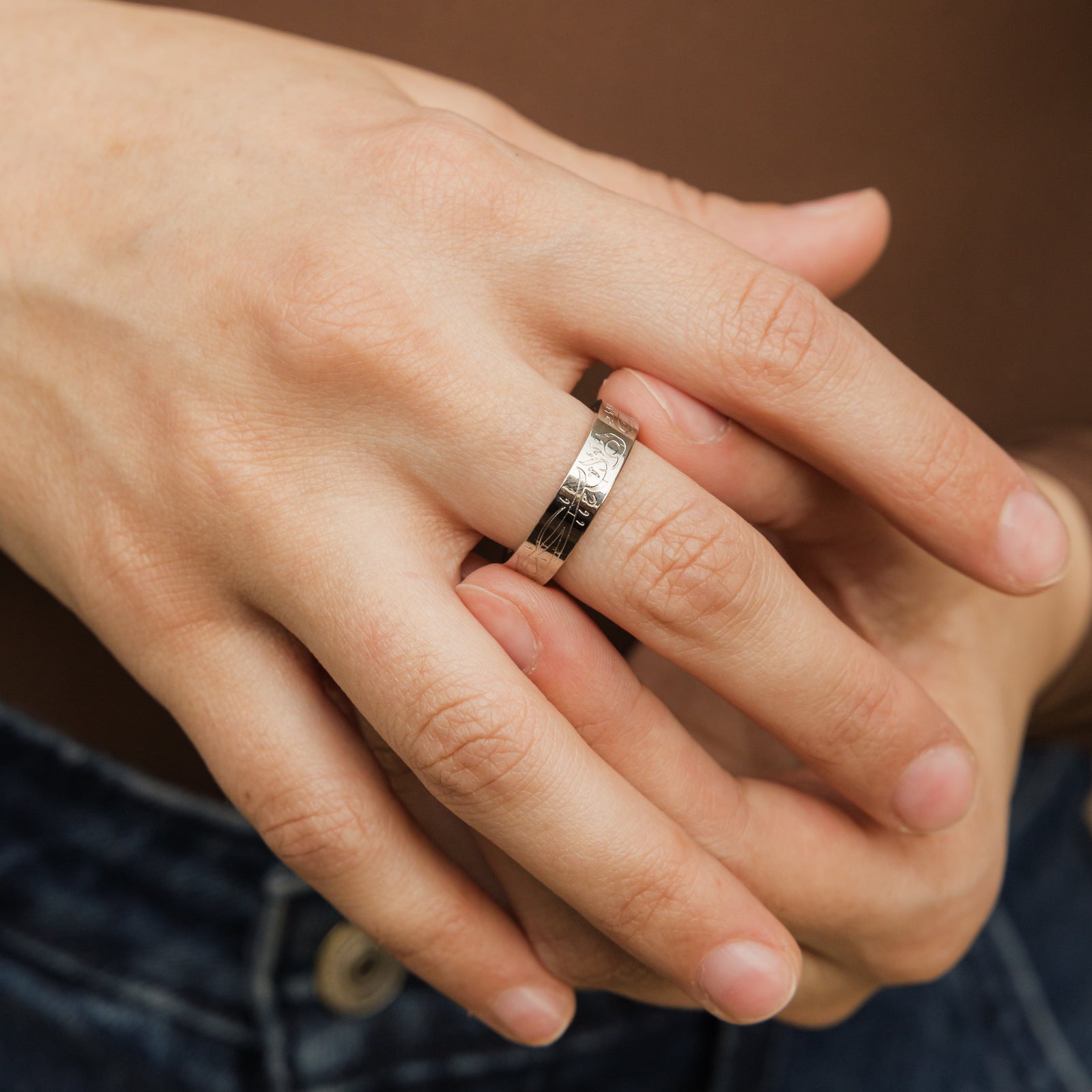 Silver Alhamdulillah ring worn on middle finger, paired with denim jeans and a brown top.