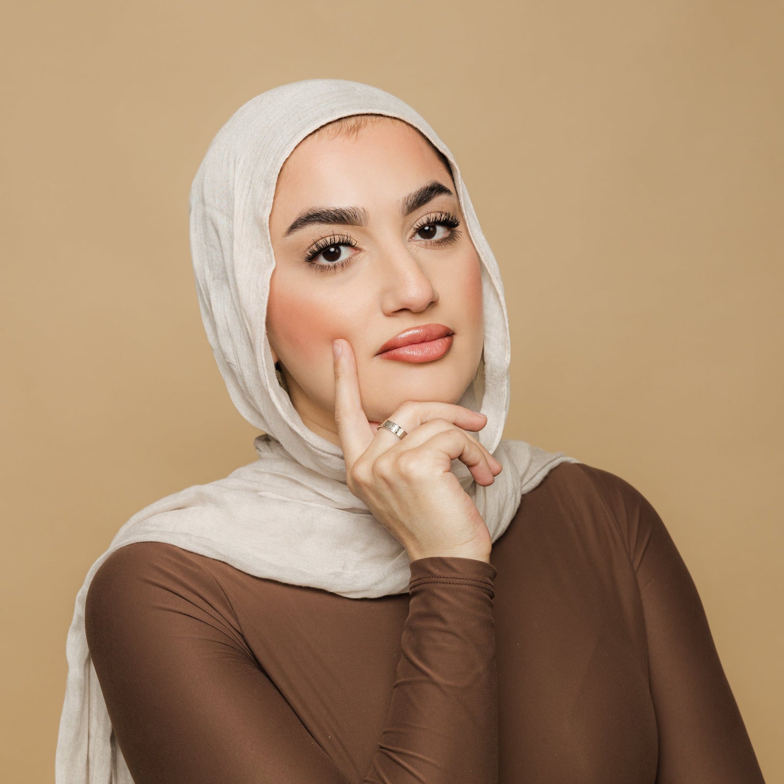 Woman wearing silver Alhamdulillah ring on her middle finger, styled with a beige hijab and brown top.