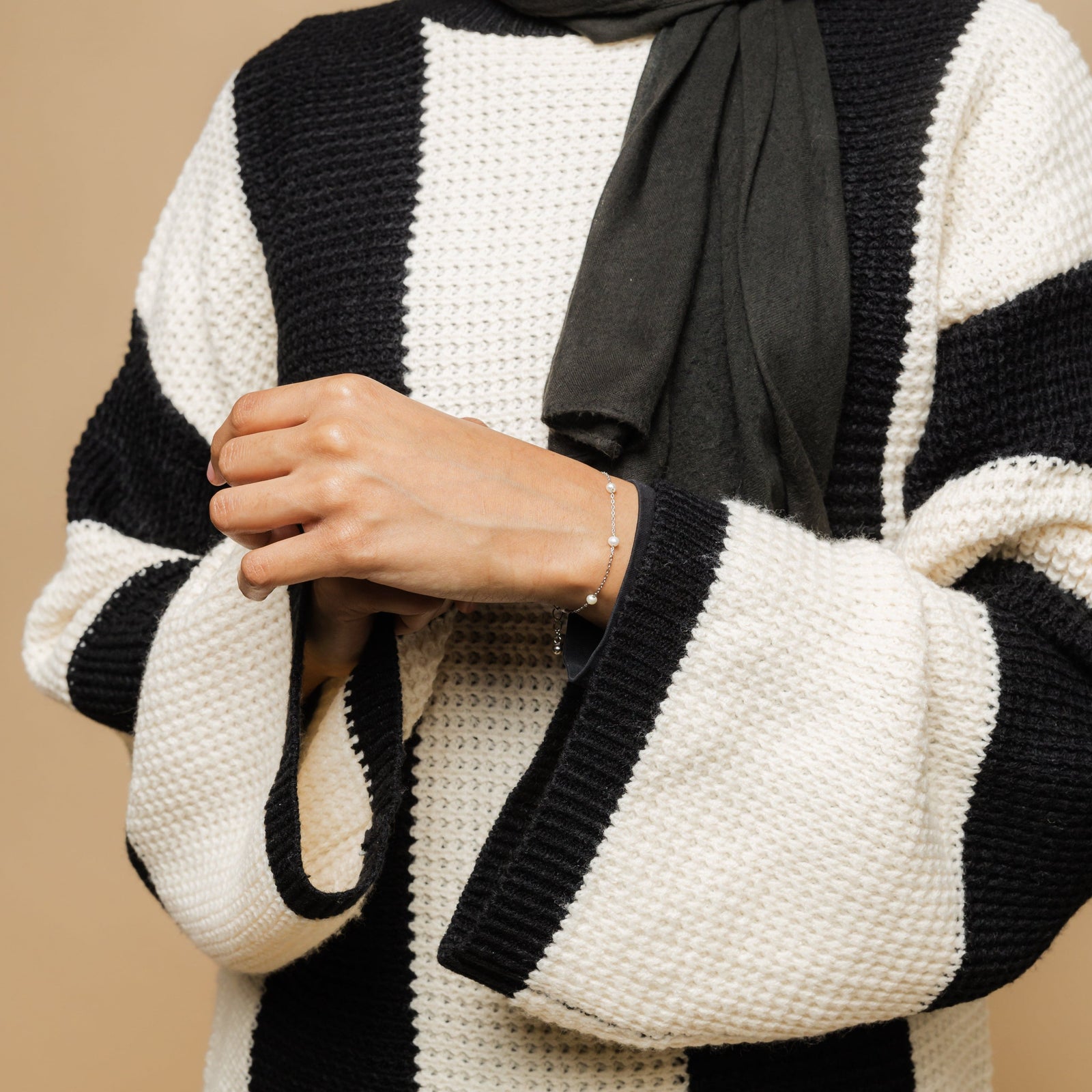 Photo of the model's hand against the white and black fabric of their clothing. The model is wearing the Pearl Strand Bracelet on their left wrist.