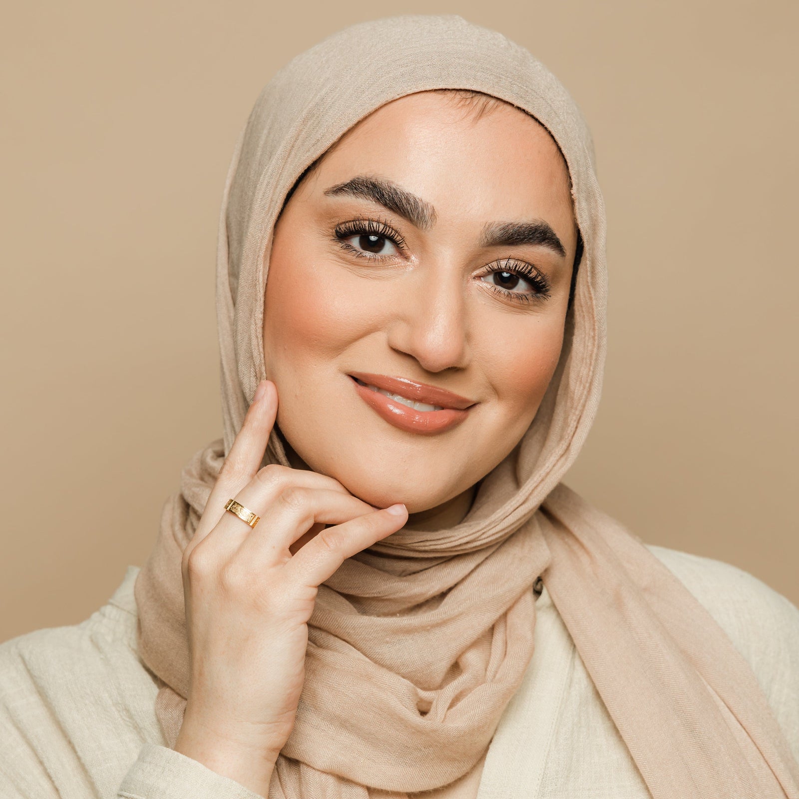 Woman wearing a beige hijab wearing the gold Five Pillars Ring on her hand, styled with a neutral-toned top.