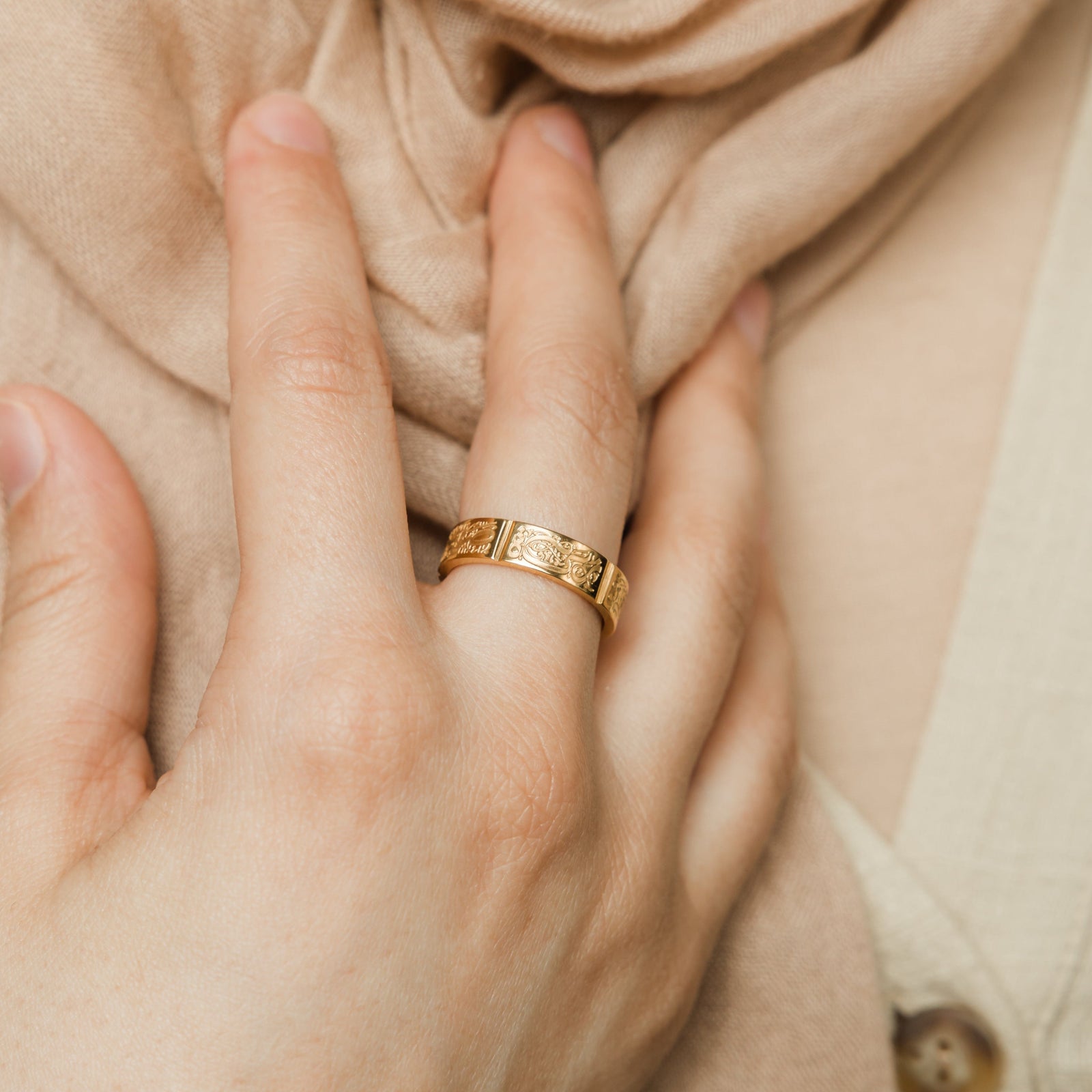 Close-up of a hand wearing the gold Five Pillars Ring, styled against a beige scarf