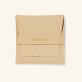 The Dangling Dotted Anklet presented in a Nominal branded beige velvet drawstring pouch, underscoring the elegant and protective packaging accompanying the jewelry piece.