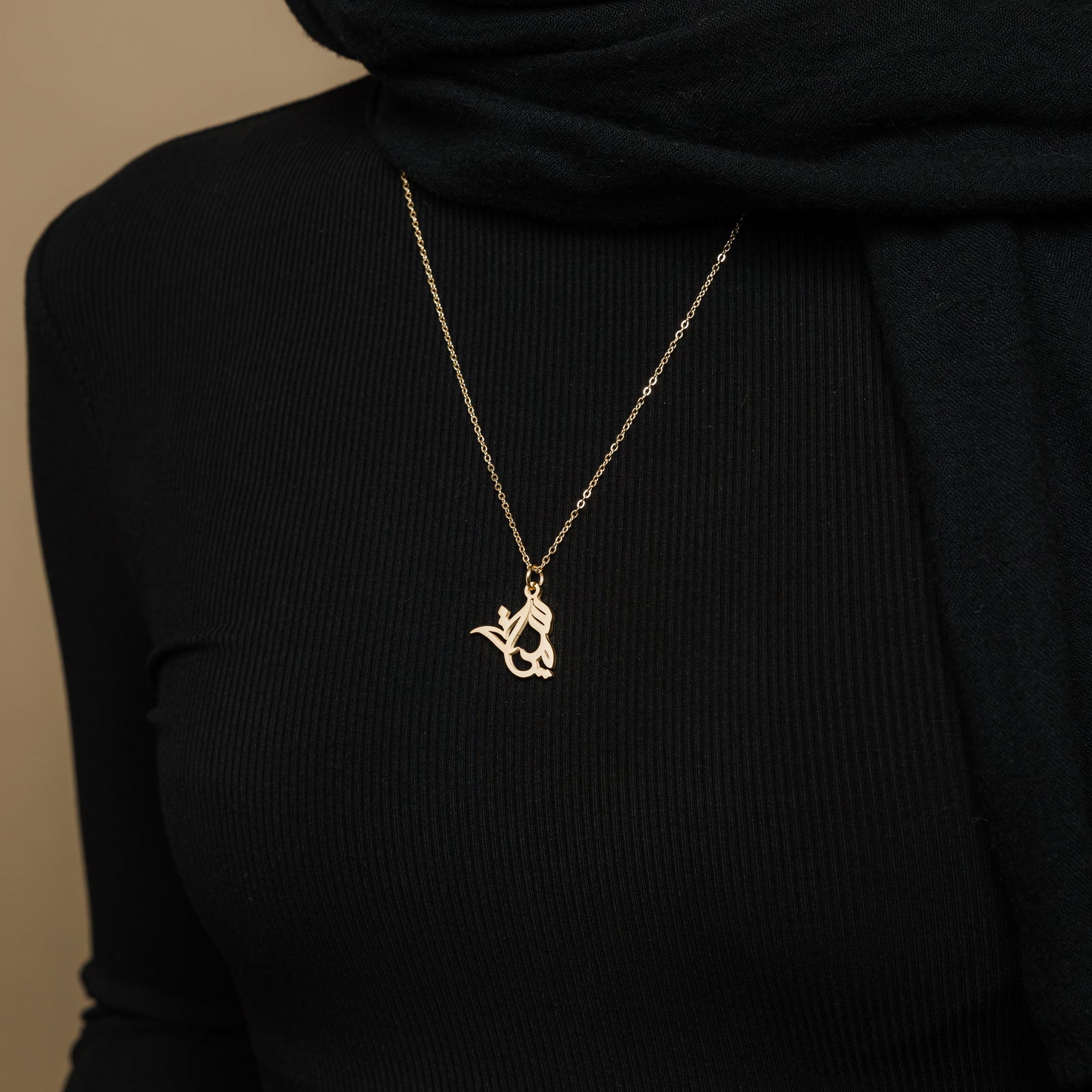 the gold Ready Calligraphy Name Necklace against the black fabric of the model's clothing