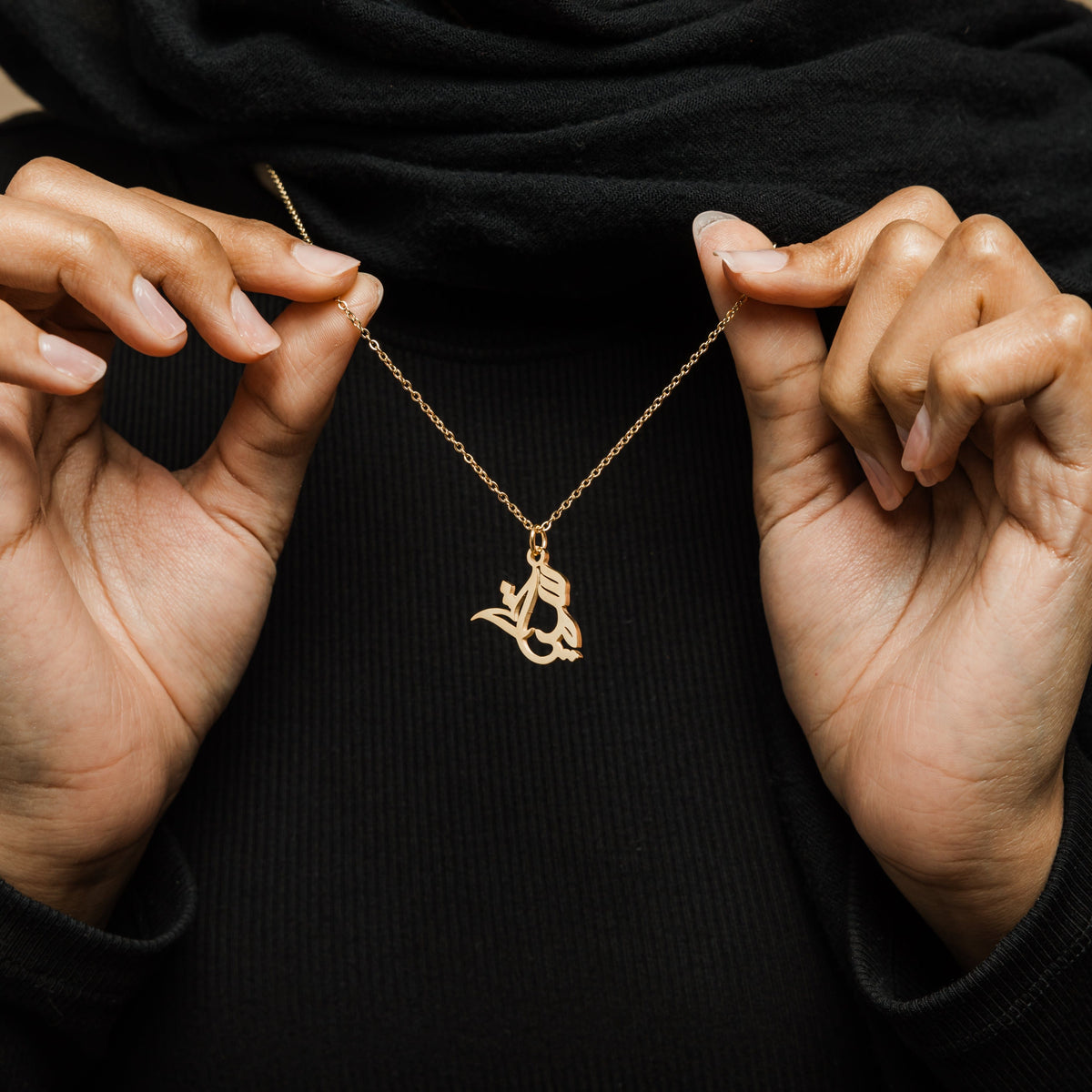 Close up of the gold Ready Calligraphy Name Necklace as the model pulls the chain to show its design.